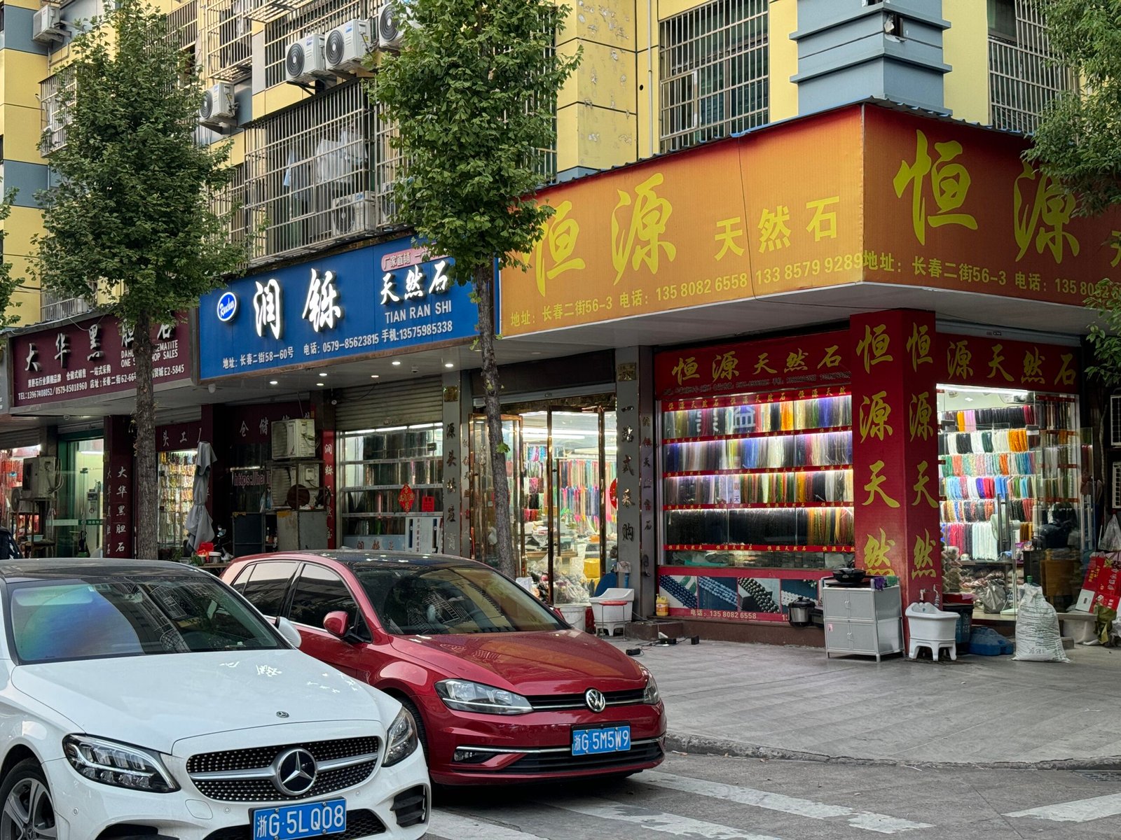 Hengyuan Natural Stone storefront with glass cases of colorful gemstone strands on Yiwu Changchun Street; amethyst, rose quartz, agate, jade, jasper; bulk orders and findings.