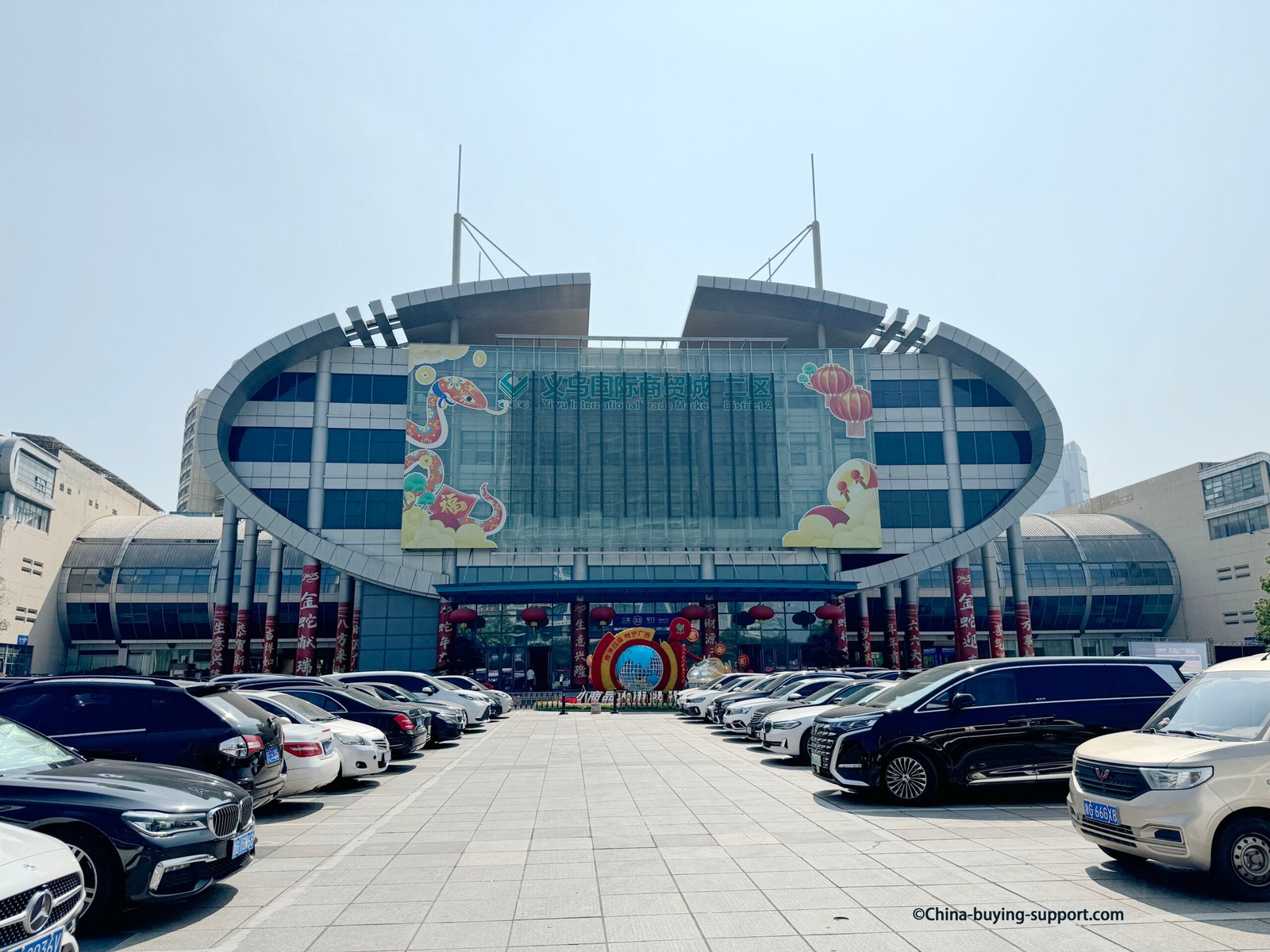 Yiwu International Trade City District 2 West Main Entrance (Gate 33) with oval glass facade, red lanterns and parked cars, Yiwu, China.