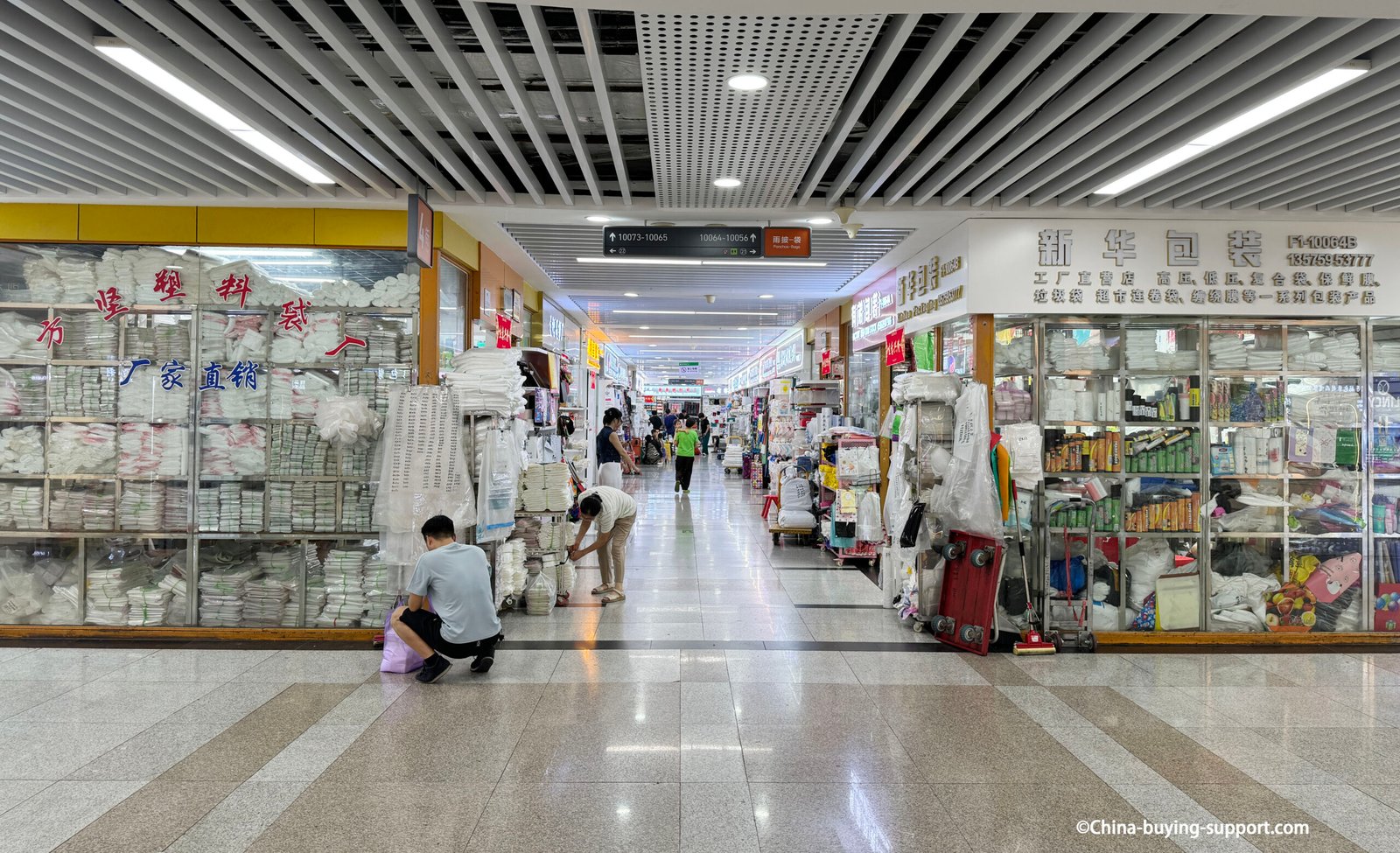 Interior view of Yiwu International Trade City District 2 packaging area with factory outlets wholesaling plastic bags, wrapping materials, and packaging supplies under bright lights in China’s largest wholesale market.