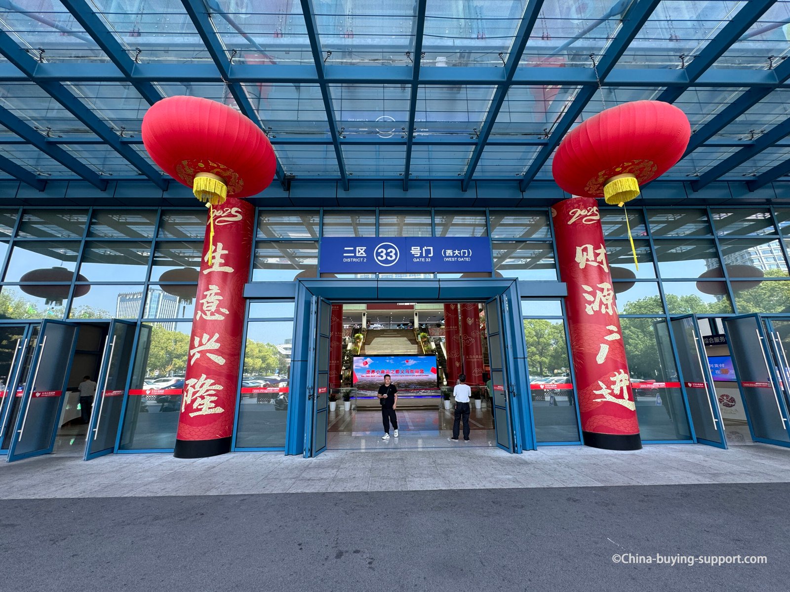 Yiwu International Trade Market District 2 Gate 33 West Entrance with red lanterns and Chinese prosperity banners, modern glass building facade in Yiwu, Zhejiang, China.
