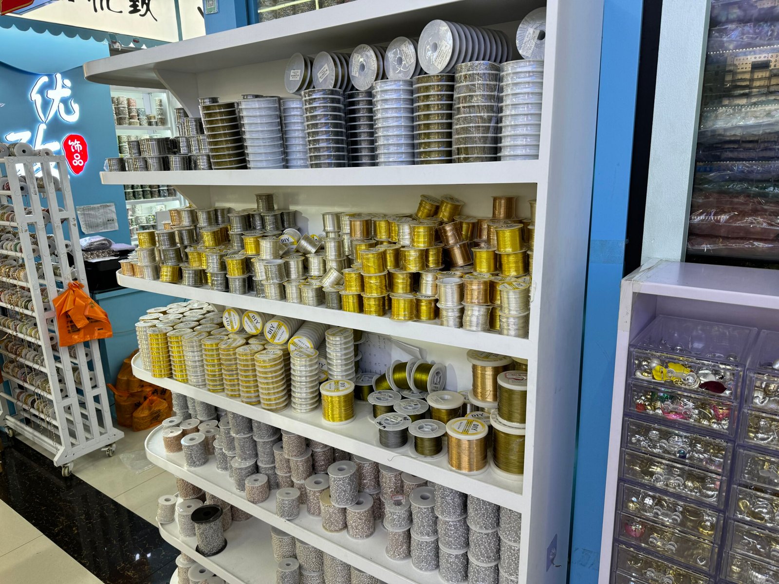 Shelves of assorted metal beading wire spools—silver, gold, brass—and elastic thread at Yiwu Jewelry Accessories Section of Yiwu International Trade City.