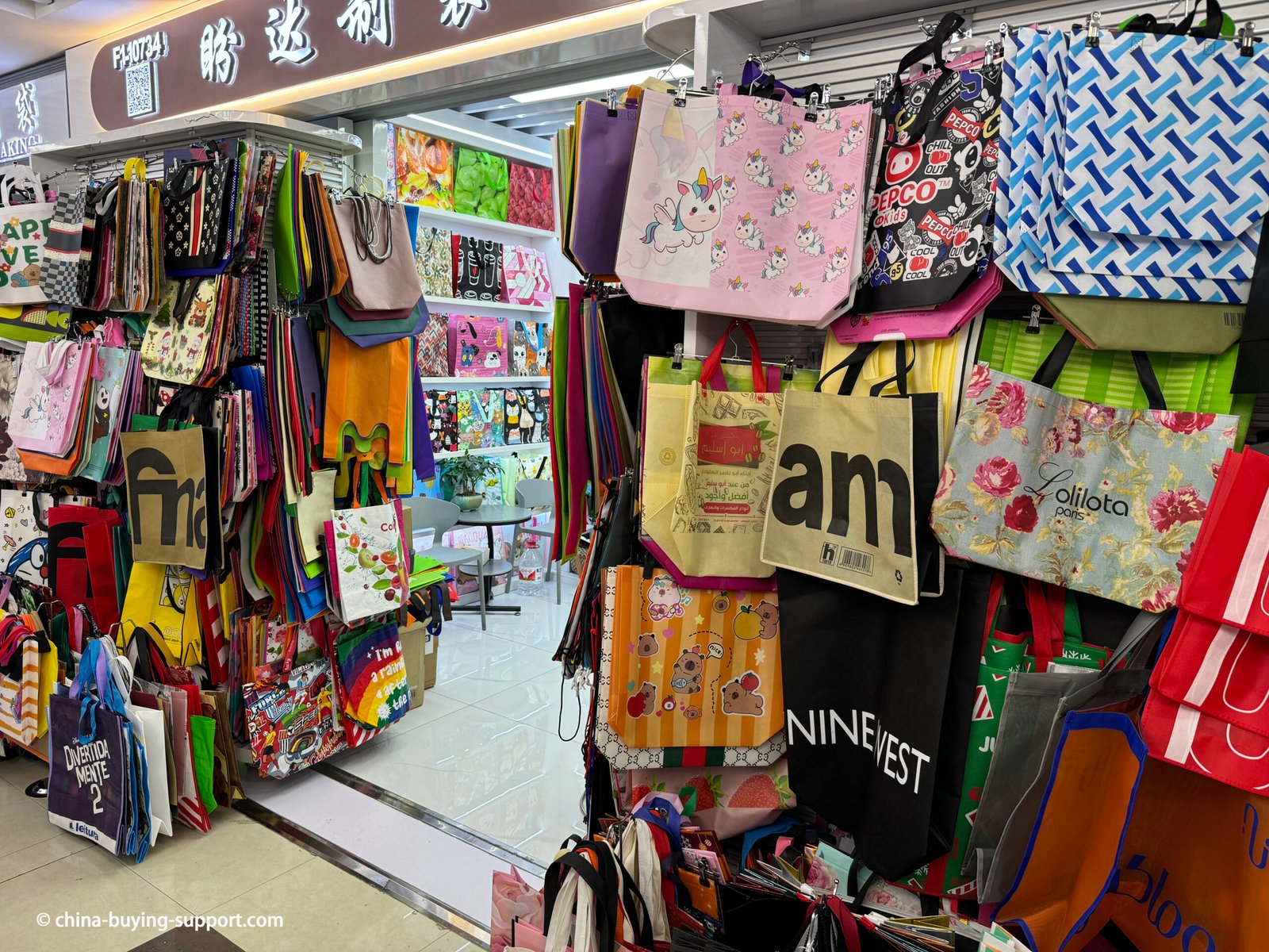 Storefront of a non-woven shopping bag supplier in Yiwu International Trade City District 2, China, displaying colorful reusable tote bags with printed designs, eco-friendly materials, and custom packaging options for wholesale buyers.