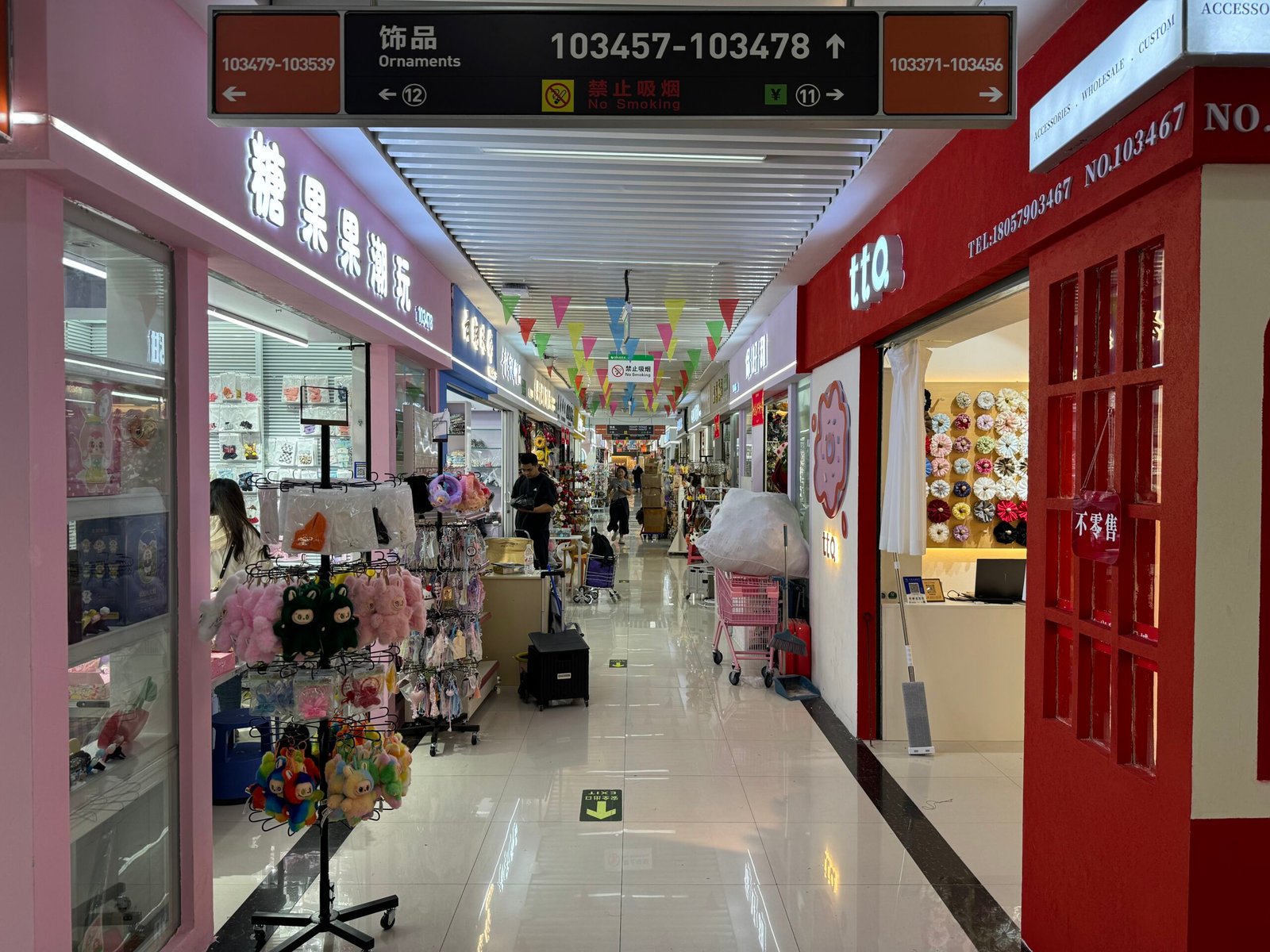Corridor of ornament shops in Yiwu with racks of hair accessories, plush keychains and display walls for DIY jewelry components.