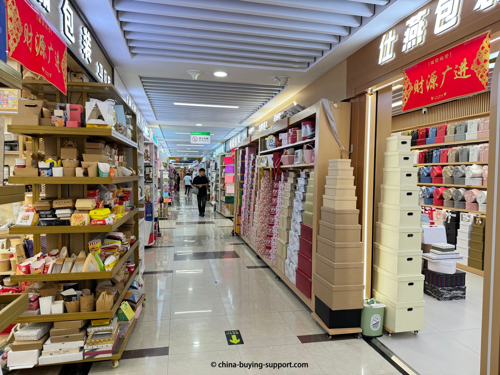Interior view of Yiwu International Trade City District 2, showing two packaging supplier shops with shelves of food boxes, gift boxes, and custom packaging materials for wholesale buyers
