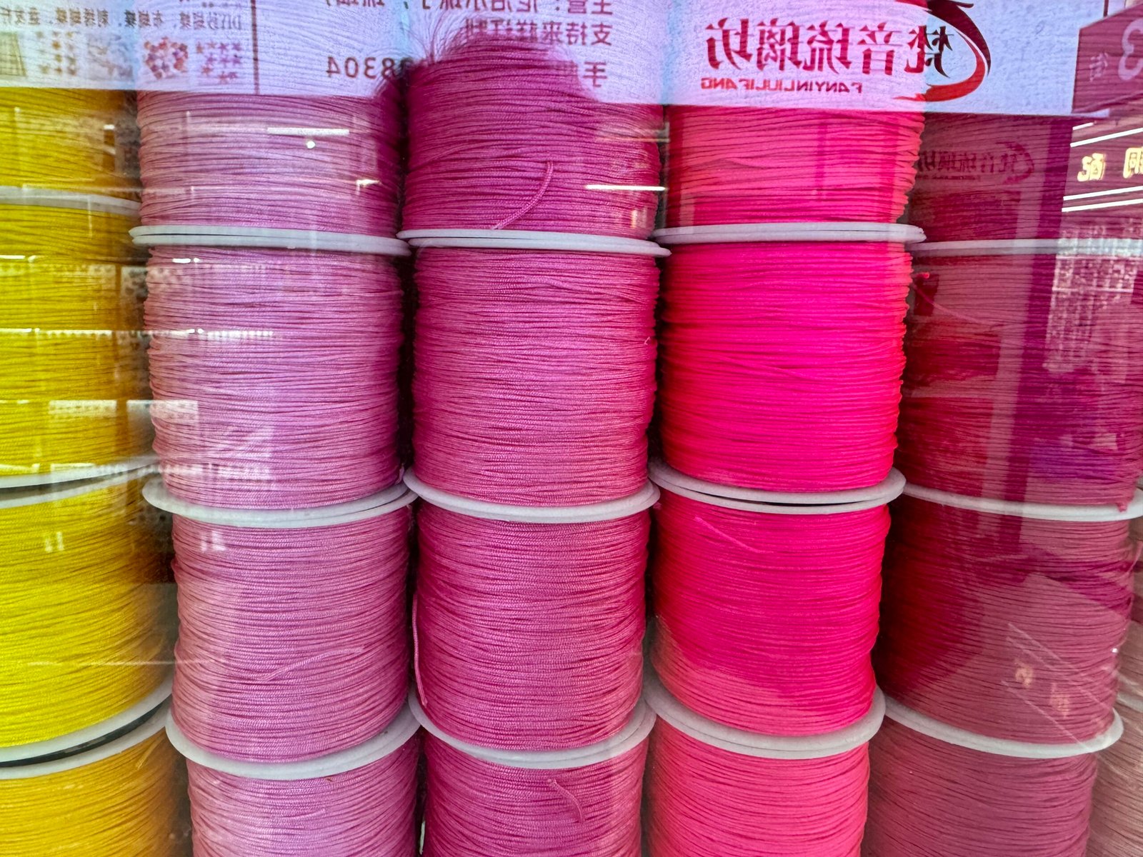 Stacks of vibrant pink nylon macramé cord spools at Yiwu accessories market.