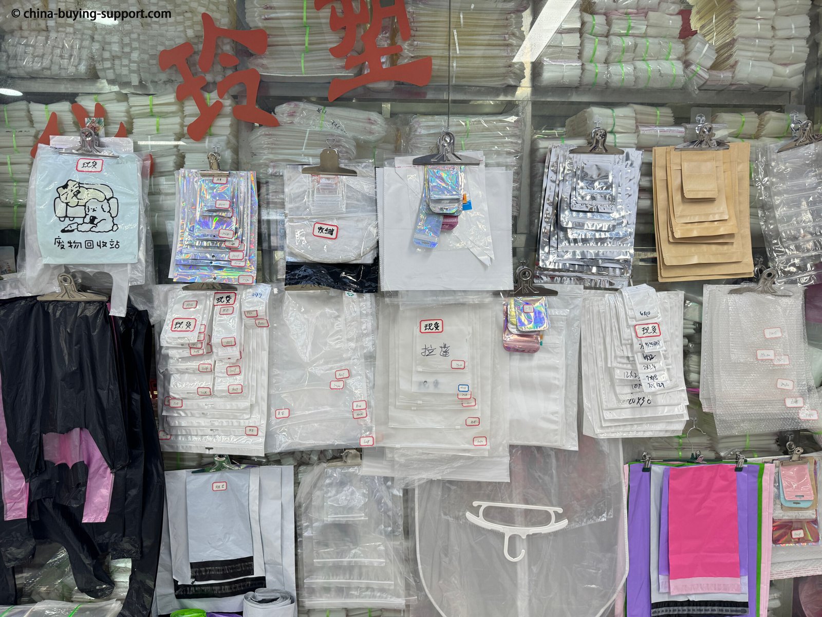 Display of various packaging bag samples at a supplier shop in Yiwu International Trade City, featuring PVC bags, OPP bags, bubble wrap mailers, zip lock pouches, courier bags, and resealable plastic packaging.