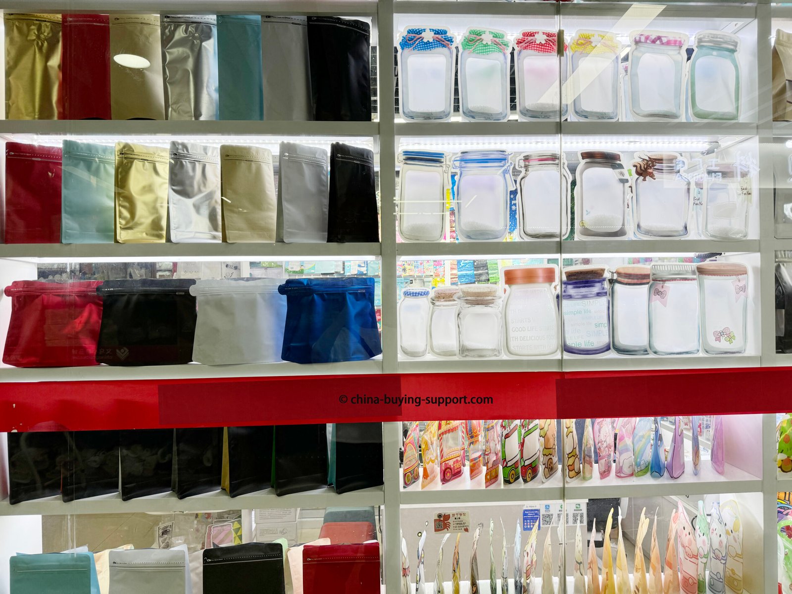 Rows of colorful PVC packaging bags and transparent plastic zipper pouches displayed on shelves at the Yiwu International Trade City Gift Packaging Market, showing a variety of bag types and materials used for product and gift wrapping