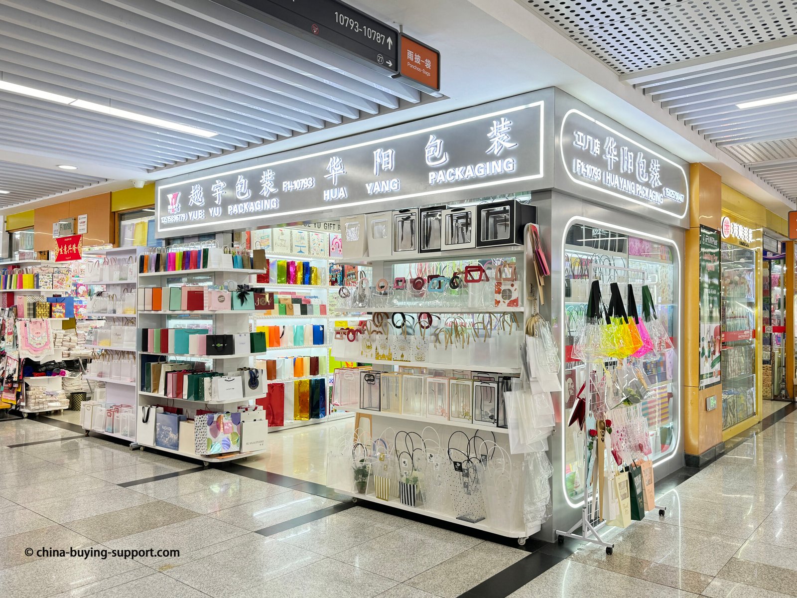 Storefront of a PVC shopping bag supplier in Yiwu International Trade City District 2, China, displaying transparent tote bags, clear PVC packaging, and custom printed gift bags for wholesale buyers.