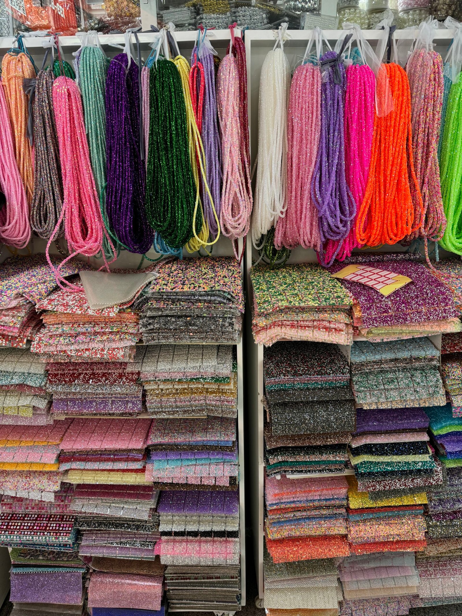 Hanging rhinestone ropes with stacked glitter and sequin fabric sheets in vivid colors at Yiwu market.
