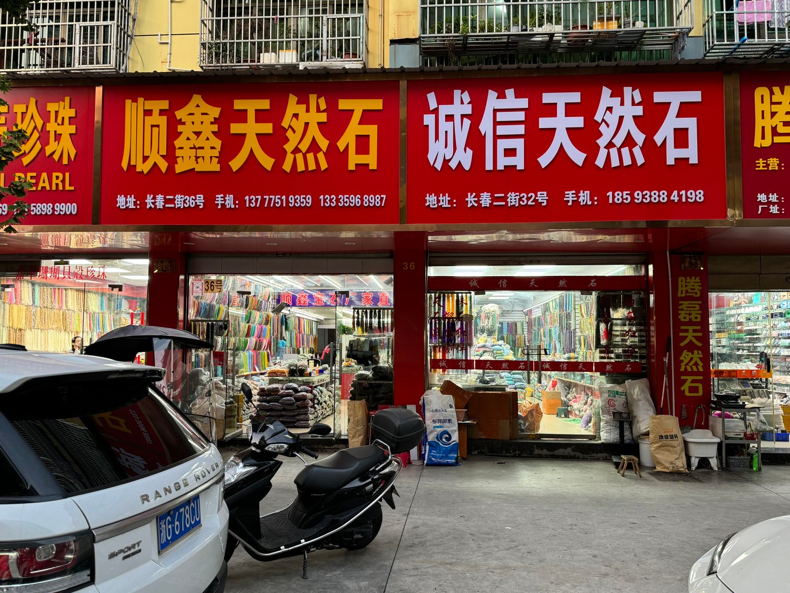 Shunxin Natural Stone and Chengxin Natural Stone storefronts packed with colorful bead strands; semi-precious gemstones and DIY jewelry hardware on display, in Yiwu Changchun Jewelry Accessories Street, China