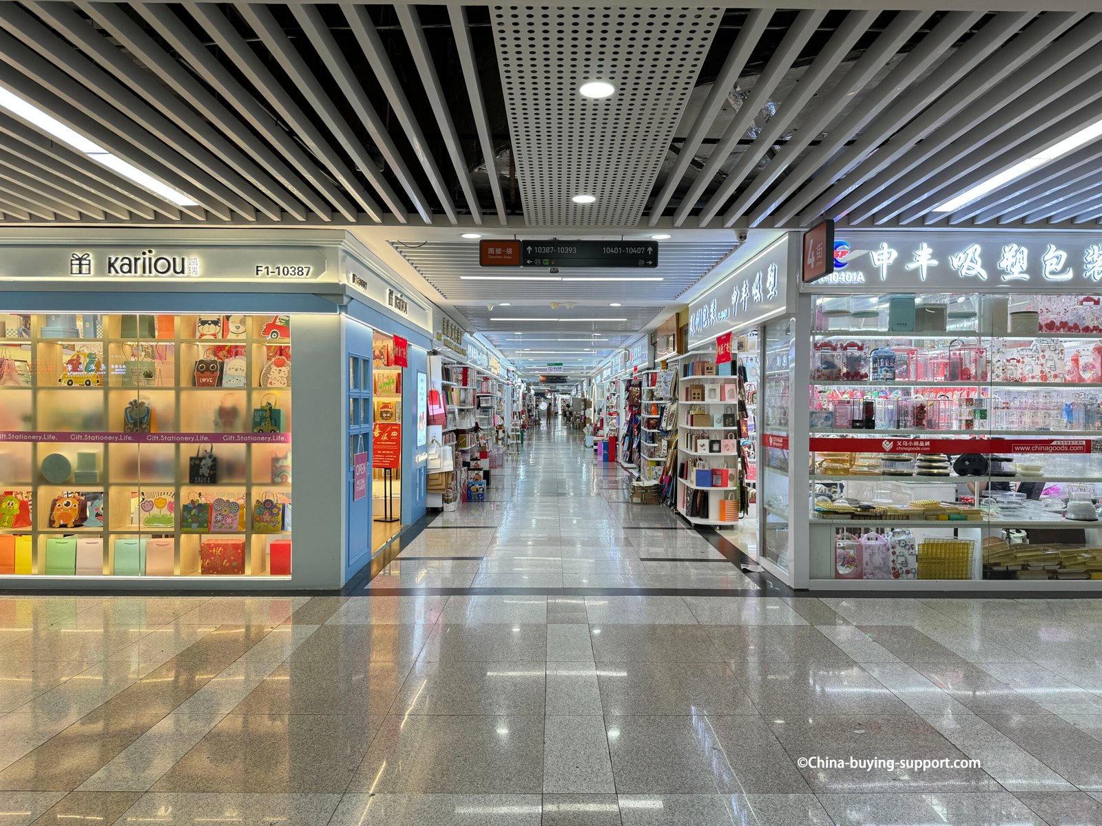 Long aisle inside Yiwu International Trade City District 2 Paper Bag and Gift Packaging Area with colorful paper bags, wrapping paper, and stationery items on display.