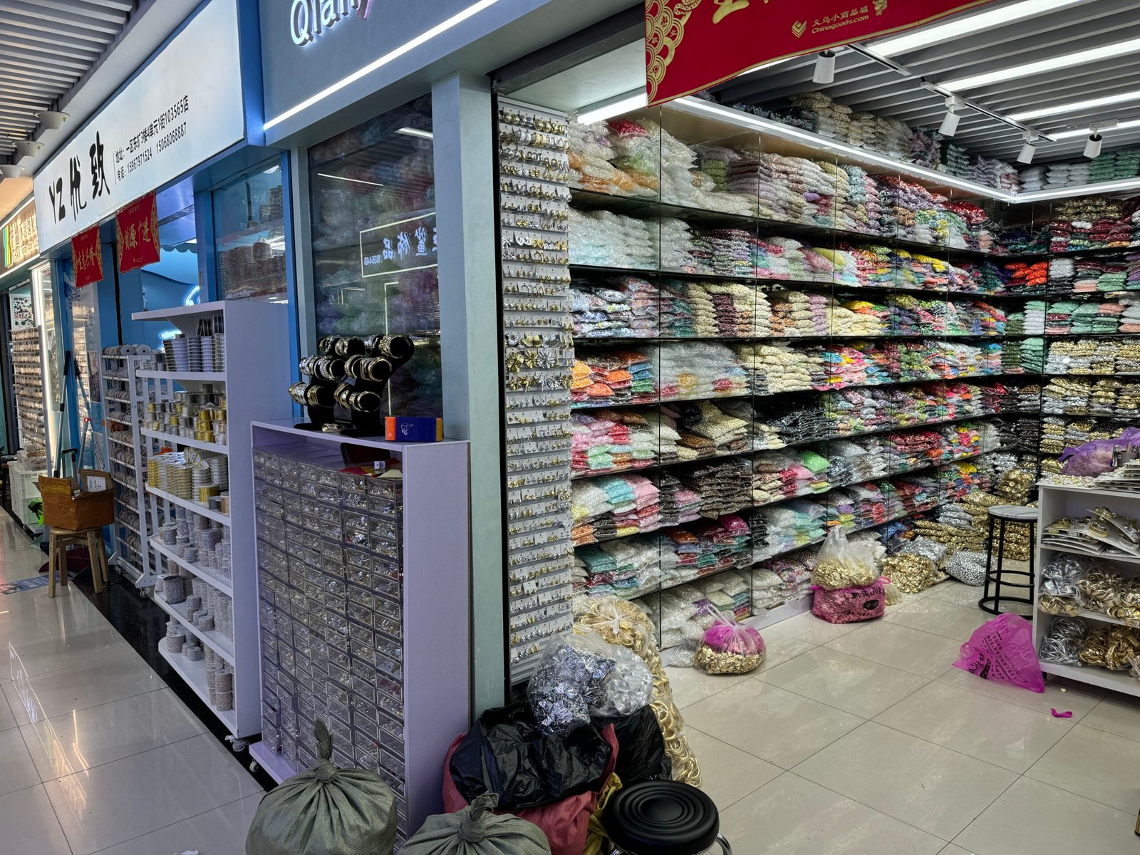 Close view of a Yiwu booth with floor-to-ceiling shelves of packaged trims and embellishments, drawers of metal findings and bracelet displays.
