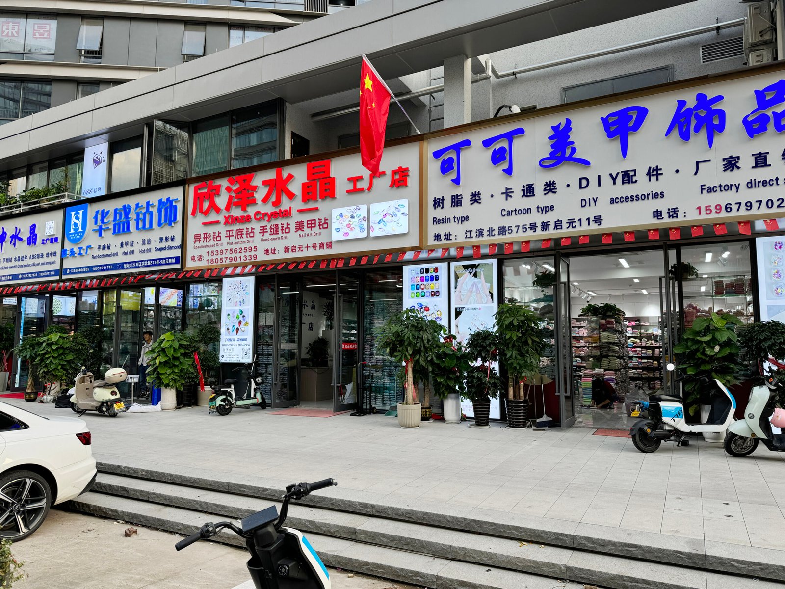 Storefront of Xinze Crystal and a nail art accessories shop with signs for flatback rhinestones, fancy stones, sew-on crystals, resin charms, cartoon pendants, and other DIY jewelry supplies, in Yiwu Xingzhong Jewelry Accessories Street