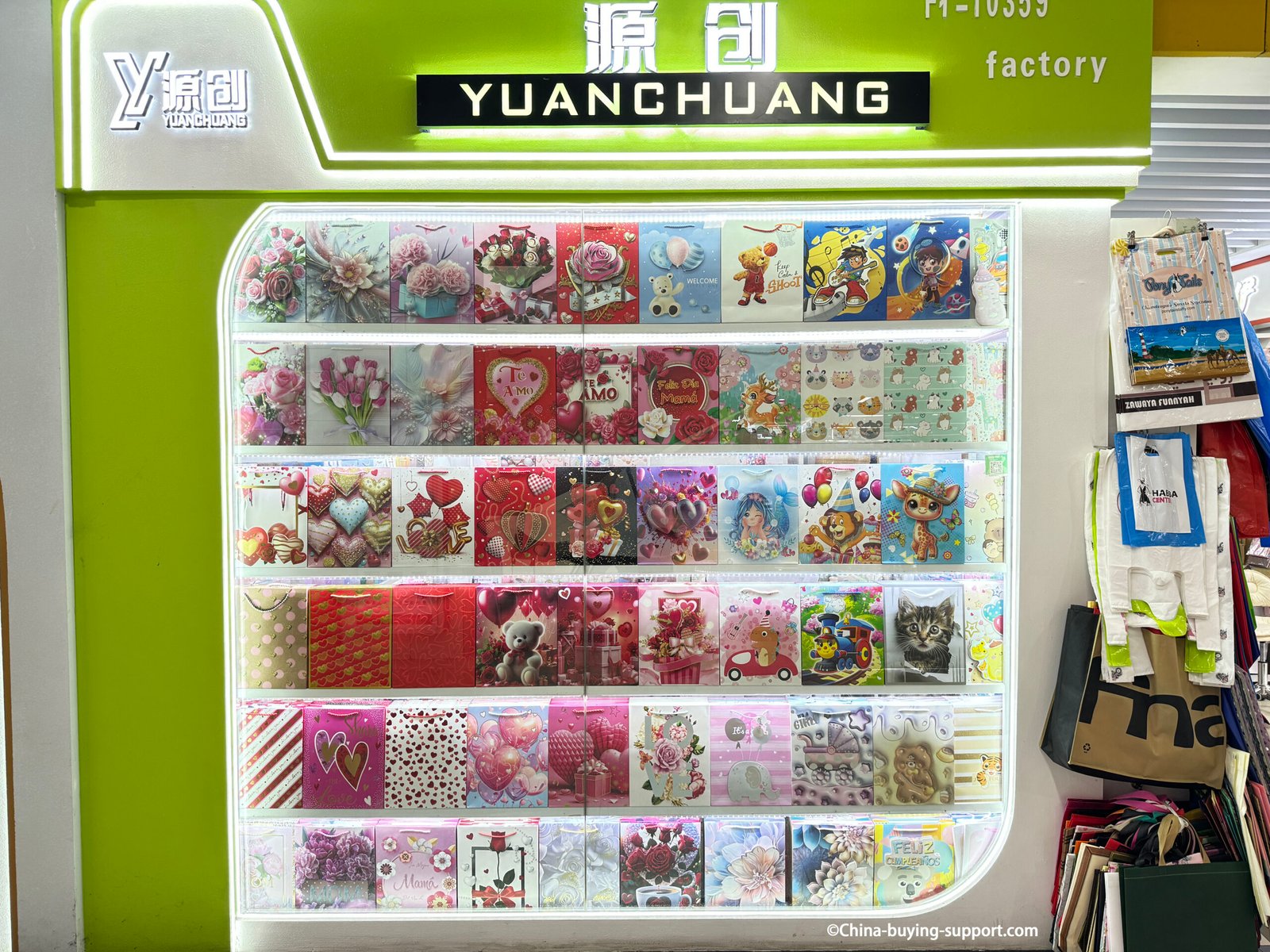 Display wall of Yuanchuang paper gift bags at Yiwu International Trade City, showing floral, heart, teddy bear, and cartoon designs for various occasions.