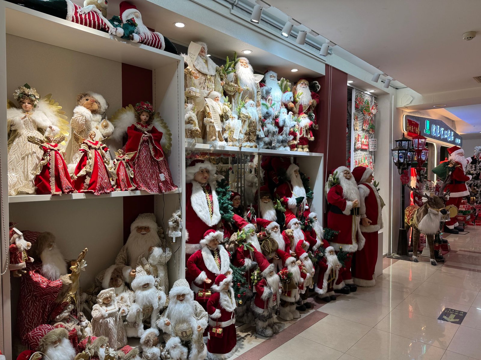 Angel figurines in red and gold dresses with classic Santa dolls on shelves in a Yiwu Christmas wholesale booth.