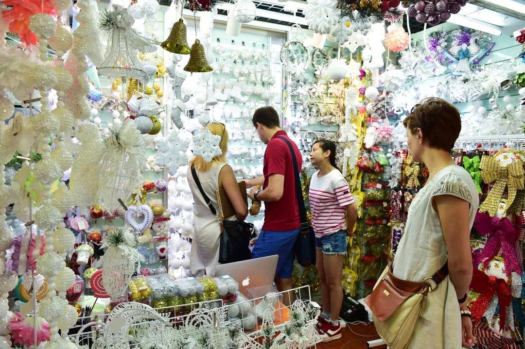 Foreign buyers browse glittering Christmas decorations inside a busy Yiwu wholesale shop, discussing orders with a local supplier.