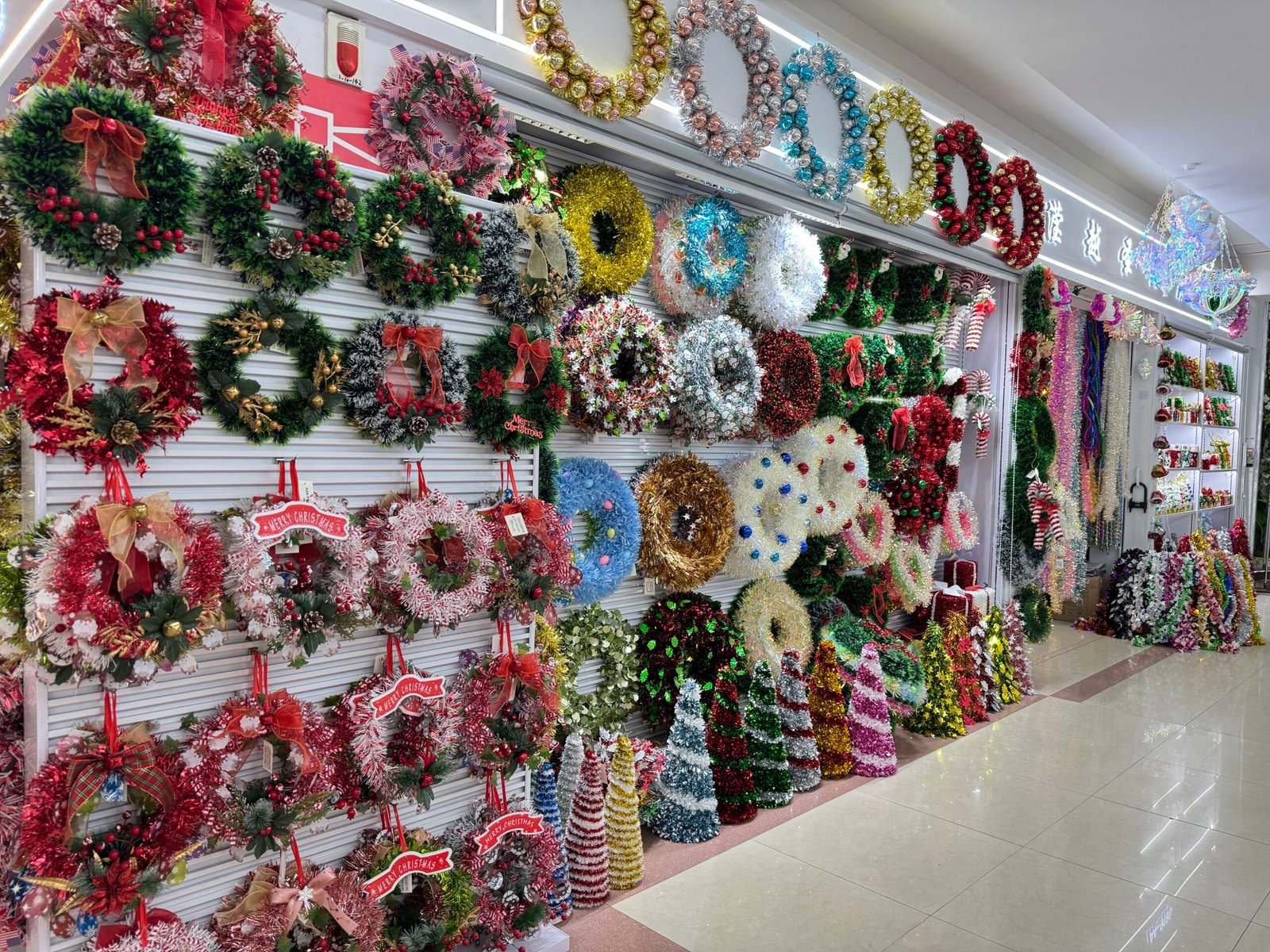 Wall display of Christmas wreaths and tinsel cone trees at a Yiwu Christmas wholesale decorations shop
