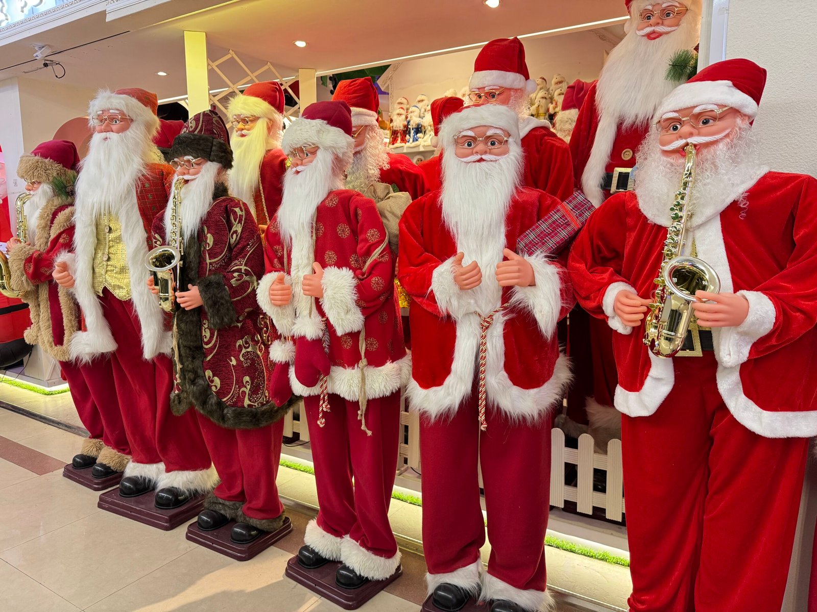 Life-size Santa Claus figures in red outfits holding saxophones lined up at a Yiwu Christmas wholesale booth.