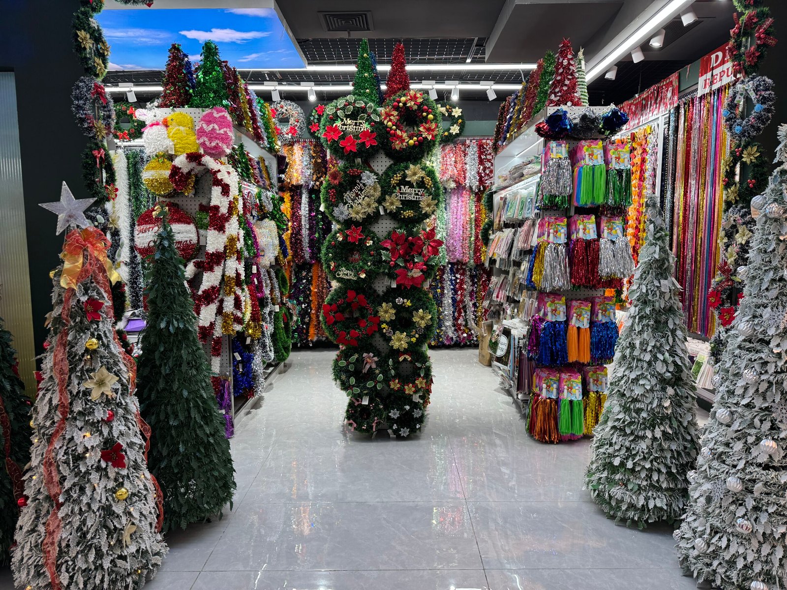 Shop entrance in Yiwu Christmas market filled with tinsel garlands, cone Christmas trees and decorative wreaths.