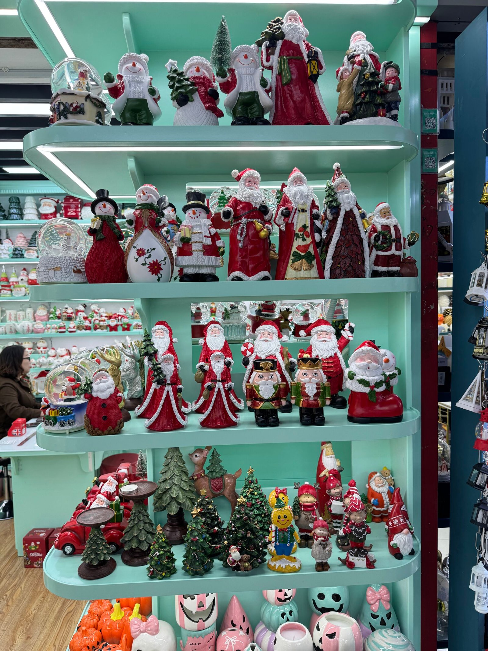 Ceramic Santa, snowman, nutcracker and Christmas tree figurines arranged on mint-green shelves at a Yiwu Christmas wholesale store.