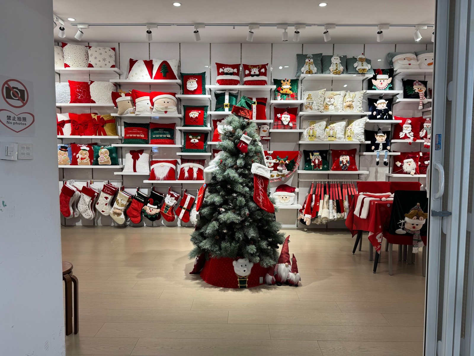 Christmas cushions and stockings covering the back wall of a Yiwu textiles decor shop with a Christmas tree in the center.