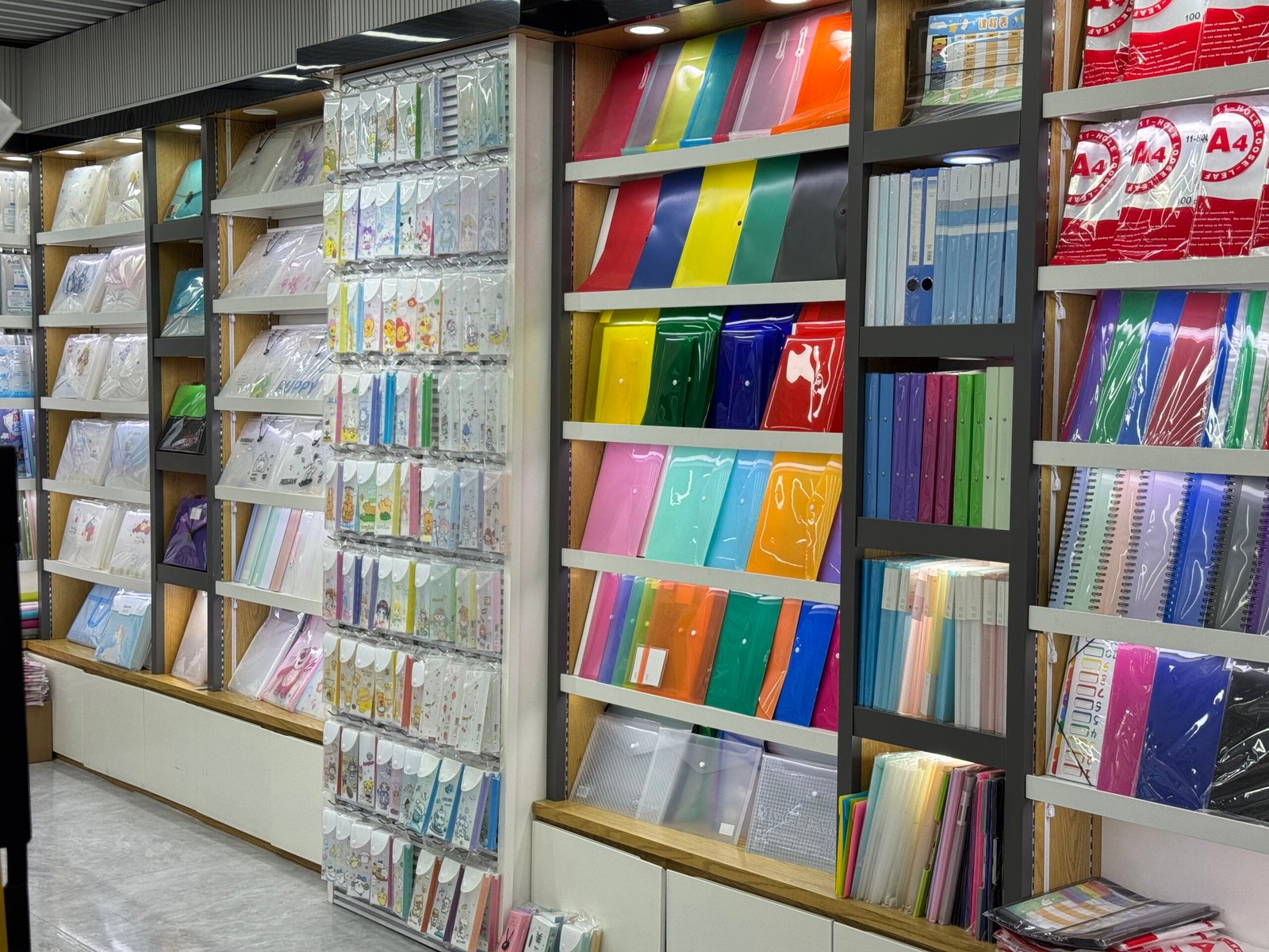 Wall shelves displaying assorted colorful plastic document folders, clear sleeves and envelopes at a stationery wholesale shop in Yiwu International Trade City.
