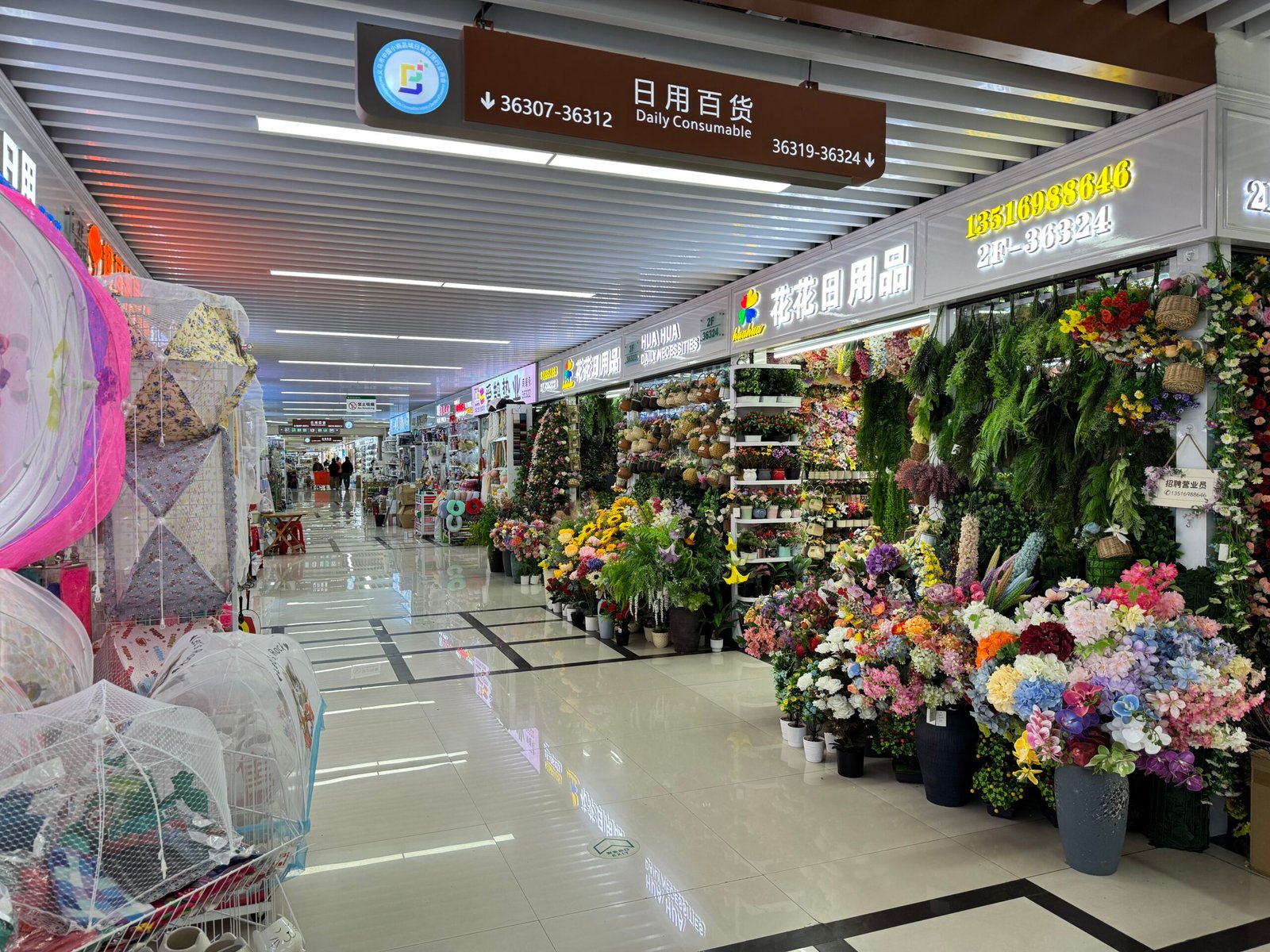 Corridor in Yiwu International Trade City District 4 Daily Consumable area lined with colorful artificial flower and plant shops displaying bouquets, wreaths and floral decorations.