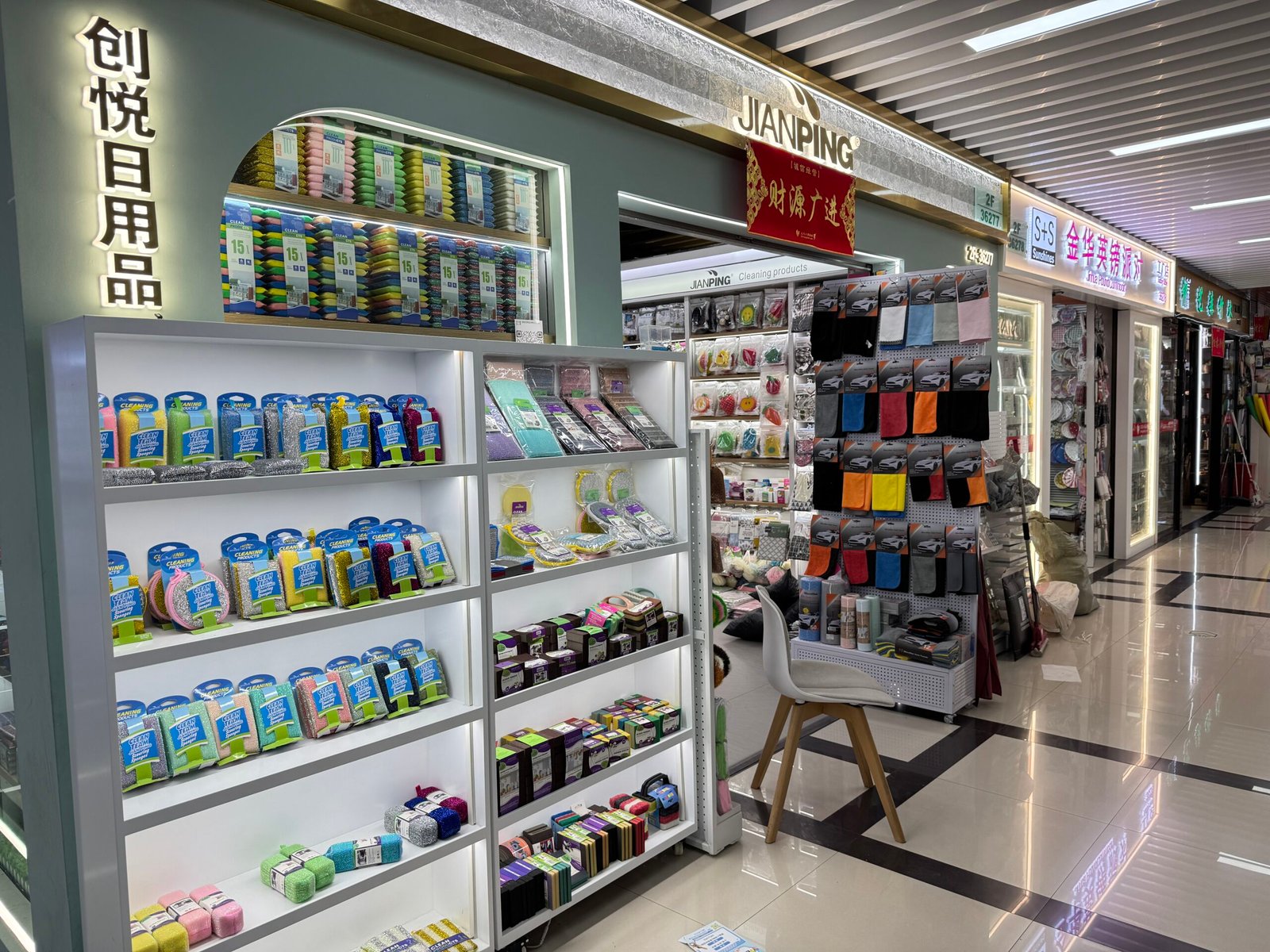 Display shelves of Jianping daily necessities shop in Yiwu International Trade City District 4 with rows of scouring pads, cleaning sponges, and colorful cloths.