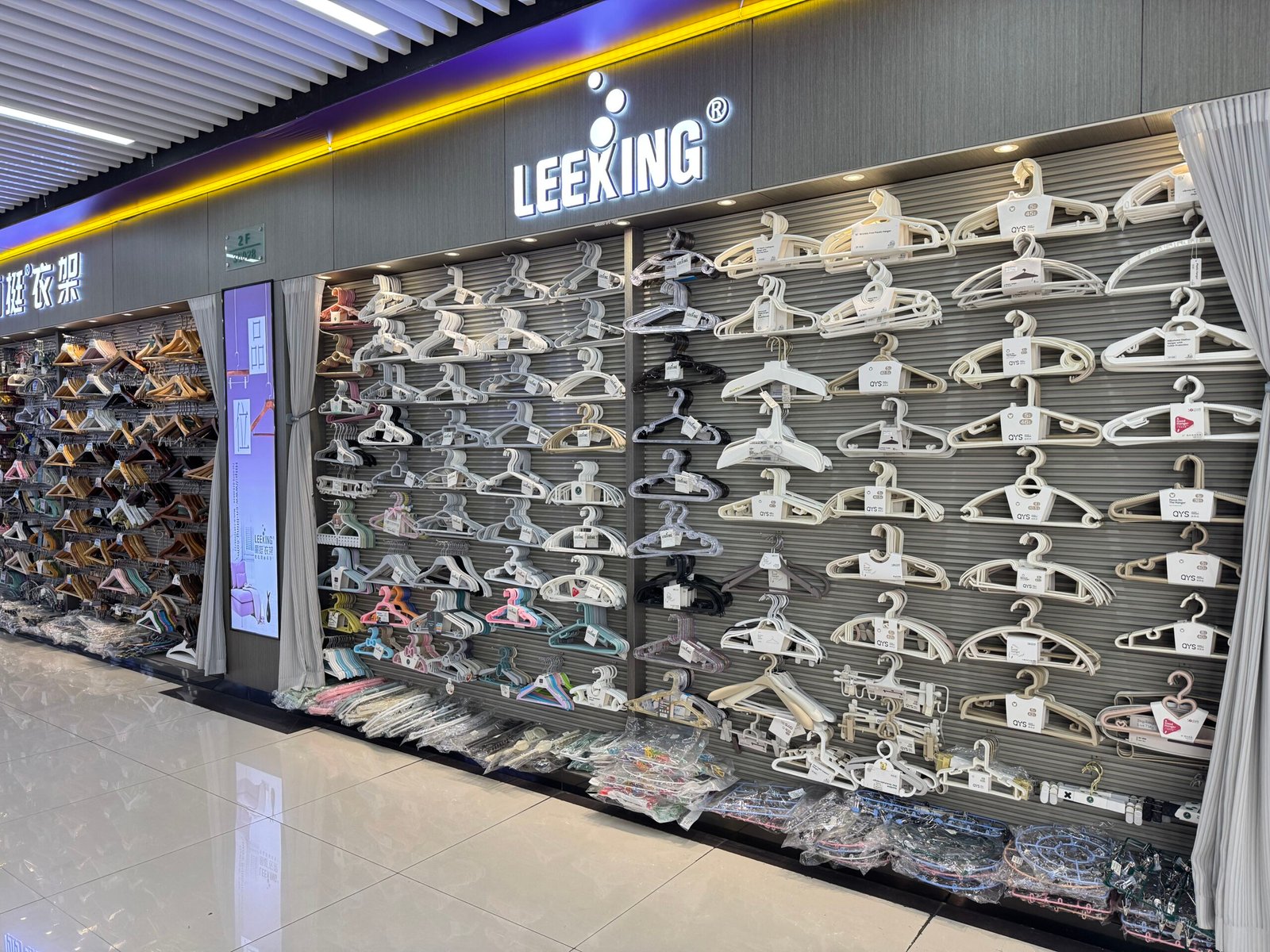 Leeking hanger showroom wall in Yiwu District 4 covered with rows of white, grey and pastel plastic hangers, with wooden hangers displayed on the adjacent wall.