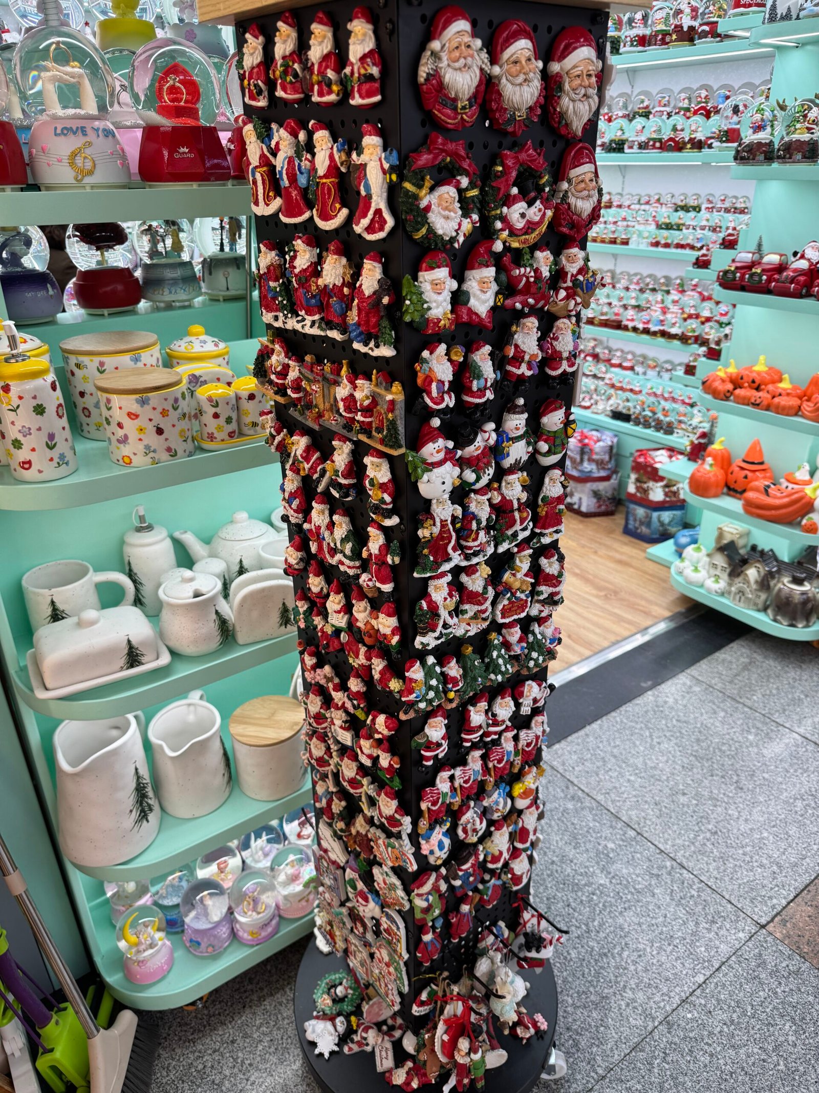 Rotating rack packed with hanging Santa ornaments in front of turquoise shelves of ceramic tableware in a Yiwu Christmas market shop.