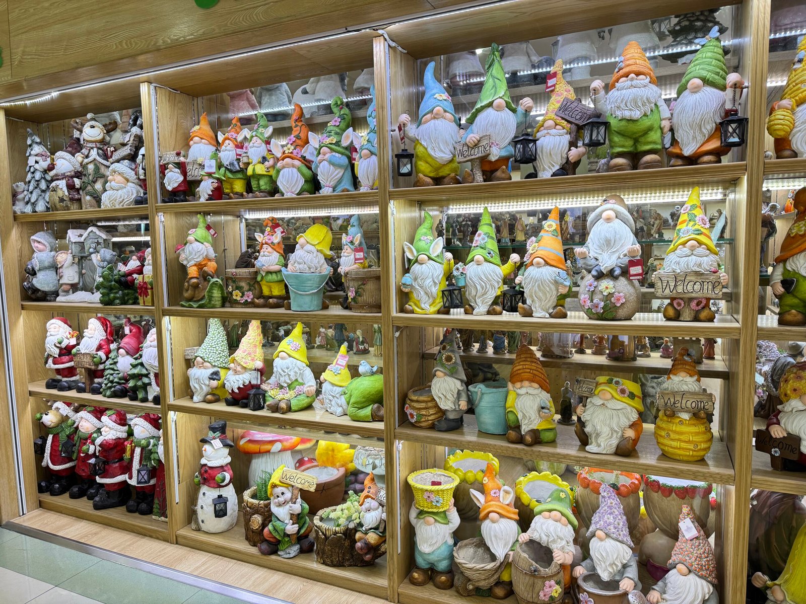Wooden display cabinet crowded with cute resin garden gnome figurines, Santa statues and seasonal ornaments inside a Yiwu wholesale home decor shop.