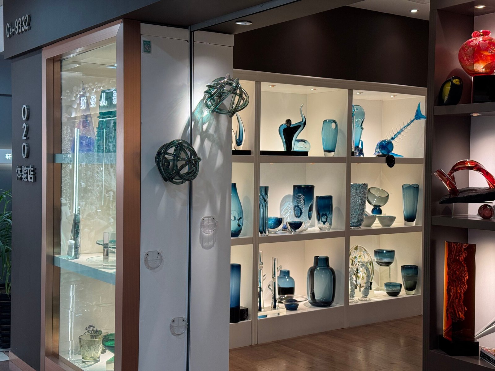 White shelving unit filled with blue glass vases, bowls, and decorative figures in a glassware store at Yiwu home decor market.