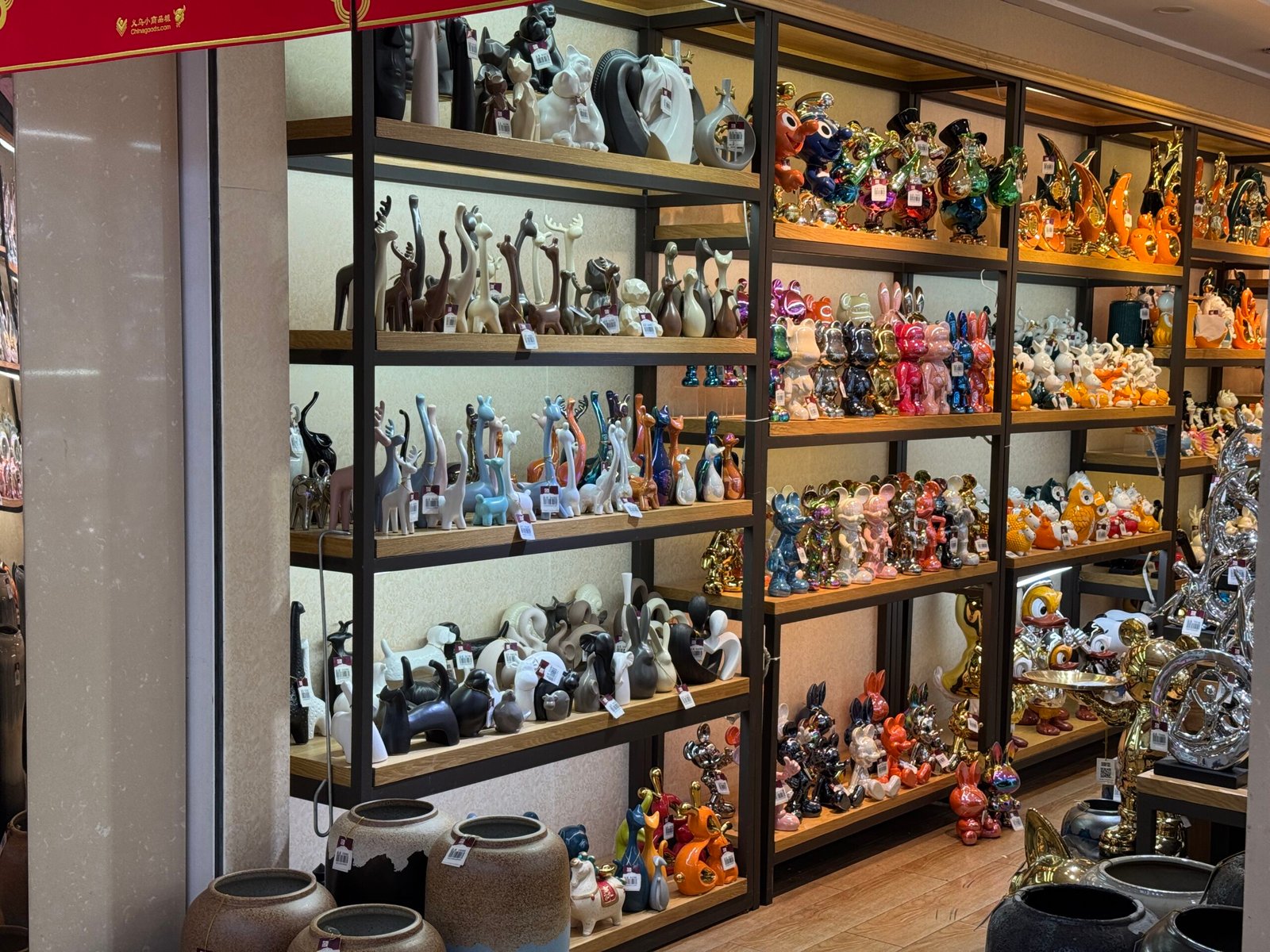 Wooden shelves stacked with ceramic deer, rabbits, and colorful cartoon animal figurines in a Yiwu home decor market stall.