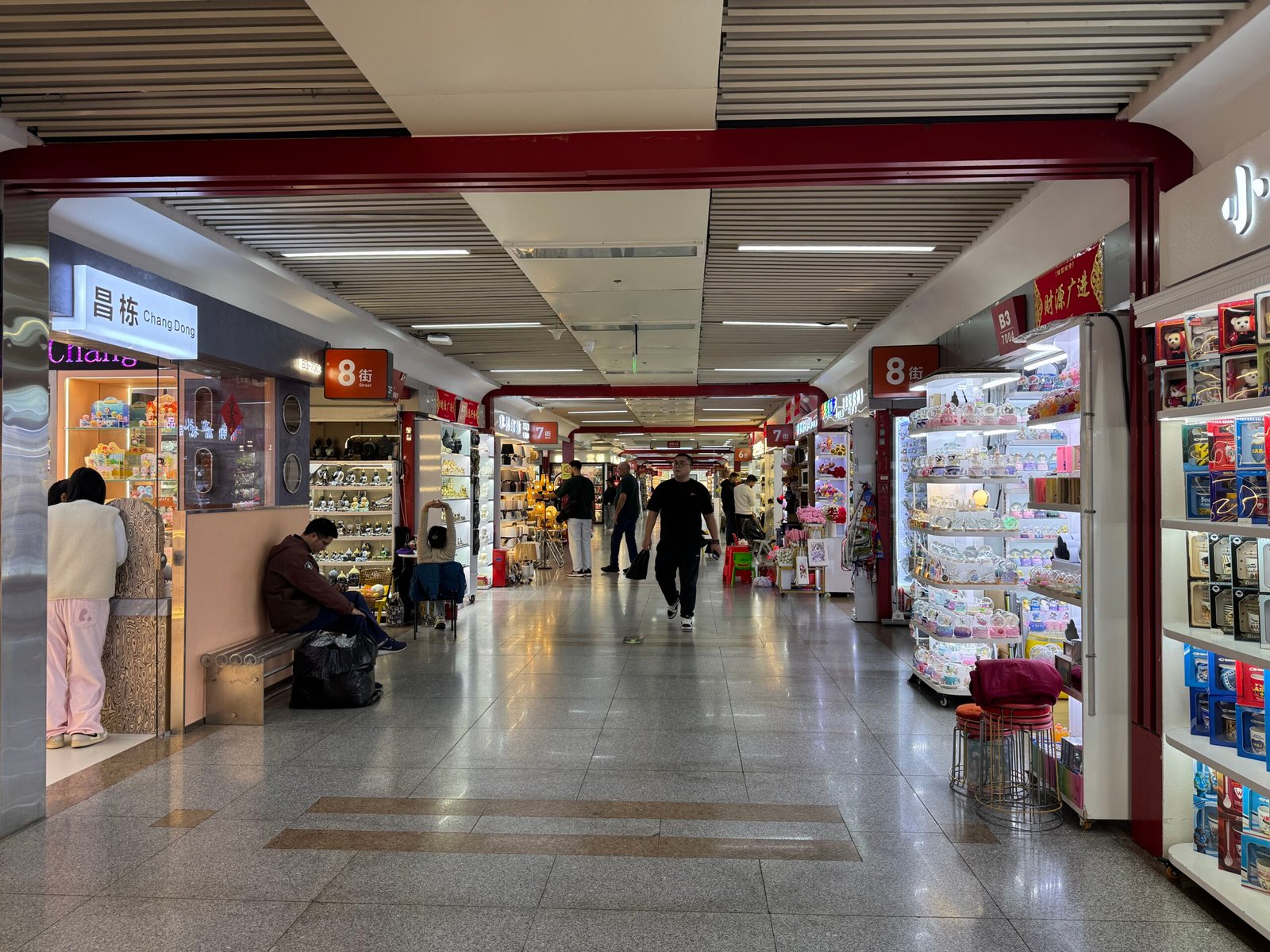 a bright indoor corridor lined with home decor and gift stalls inside the Yiwu wholesale market.