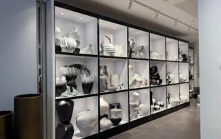 Rows of illuminated shelves in a Yiwu pottery shop filled with modern black and white ceramic vases and abstract sculptures.