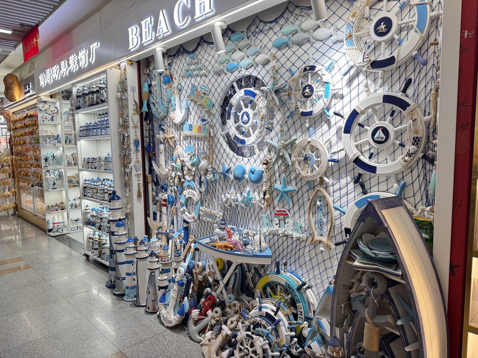 Nautical beach themed home decor stall in Yiwu market with ship wheels, starfish, shells, and lighthouses covering the front wall
