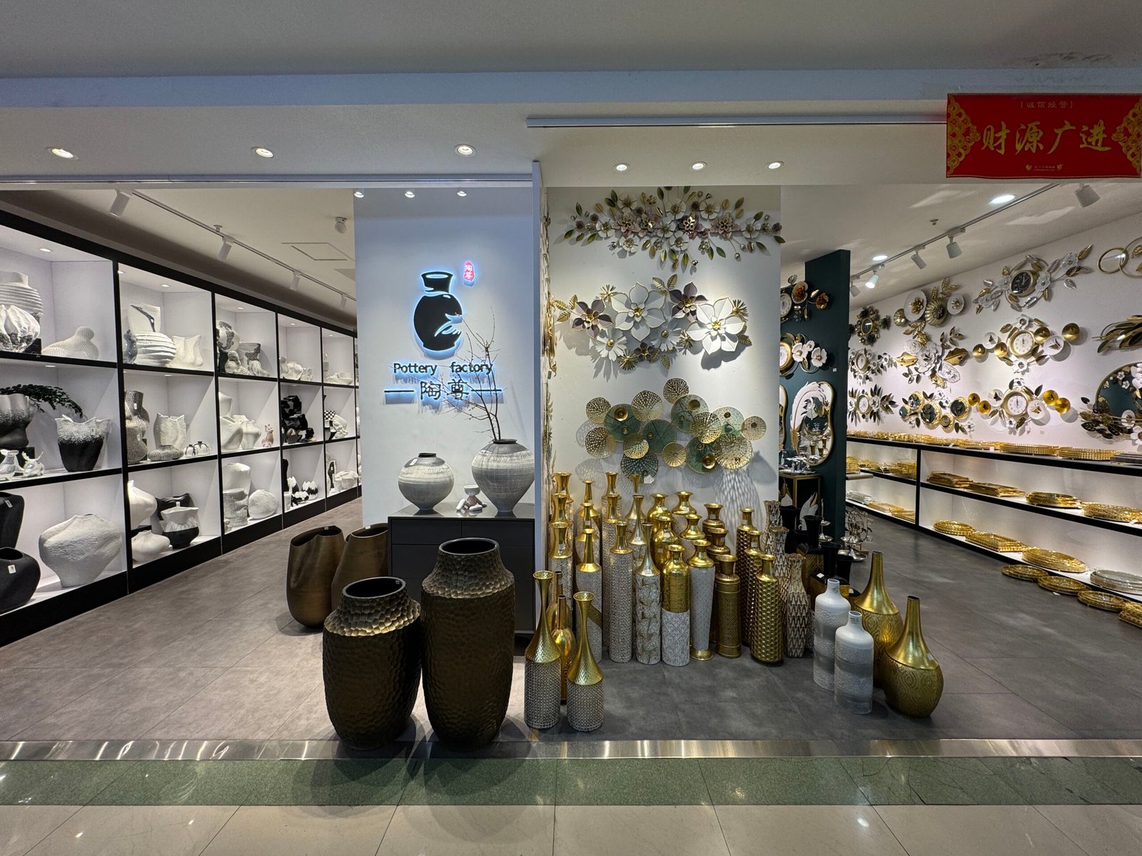 Pottery Factory storefront at Yiwu home decor market with white ceramic vases on one side and tall gold vases and decorative wall art on the other.