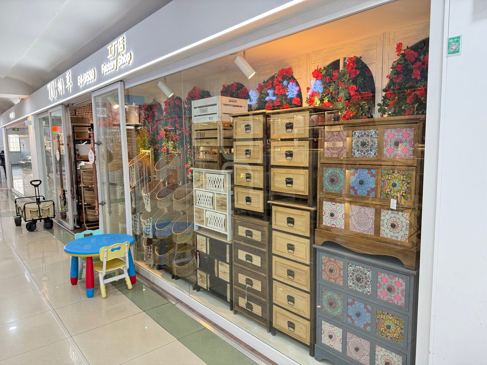 Glass-fronted factory shop in Yiwu decor market showing wooden storage cabinets with drawers, wicker baskets and rustic home organization furniture.