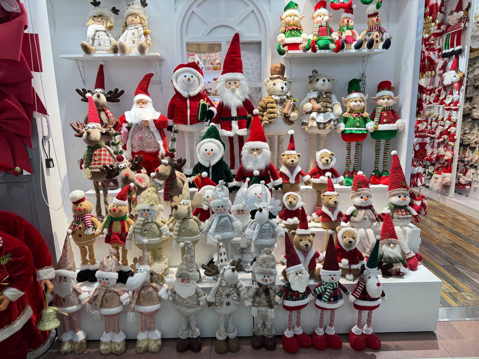 Assorted plush Christmas dolls with Santas, snowmen, reindeer, bears and elves displayed on white steps in a Yiwu wholesale booth.