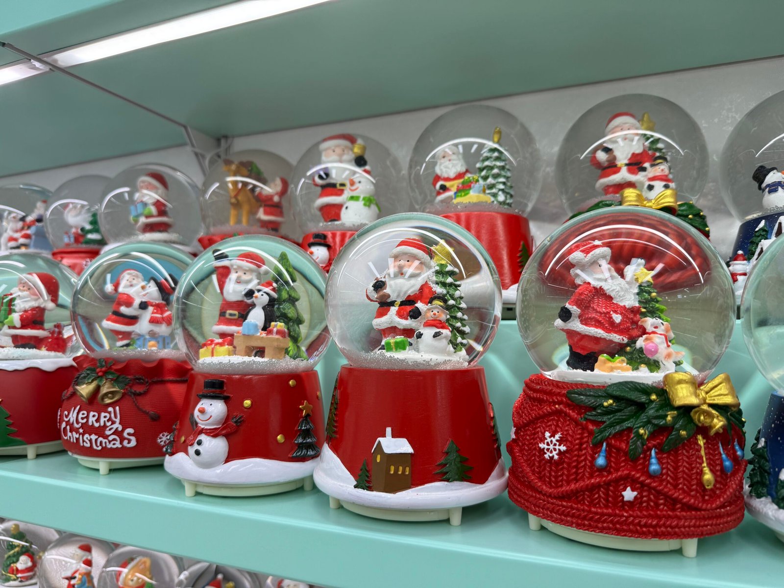 Close view of large Christmas snow globes showing Santa figures and winter scenes on red bases in a Yiwu wholesale shop.