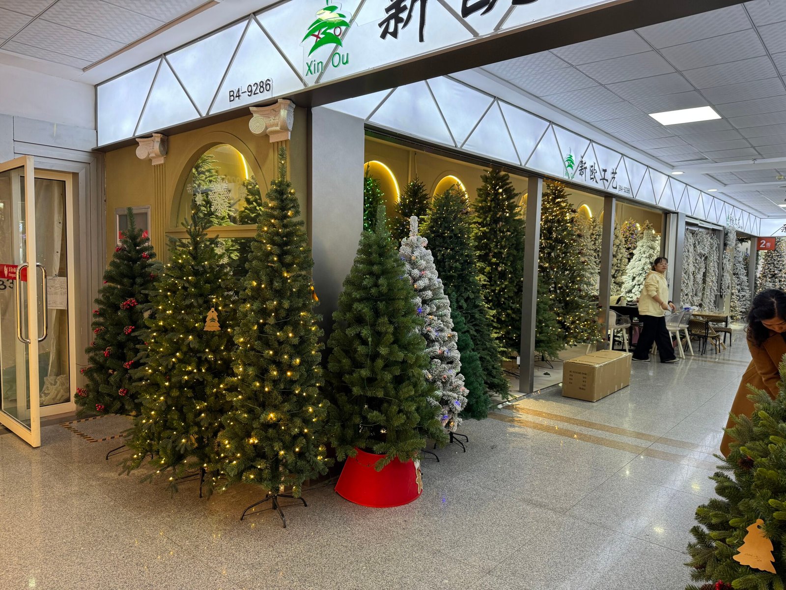 Yiwu Xin Ou Christmas showroom with rows of artificial Christmas trees in various heights and snow-flocked finishes.