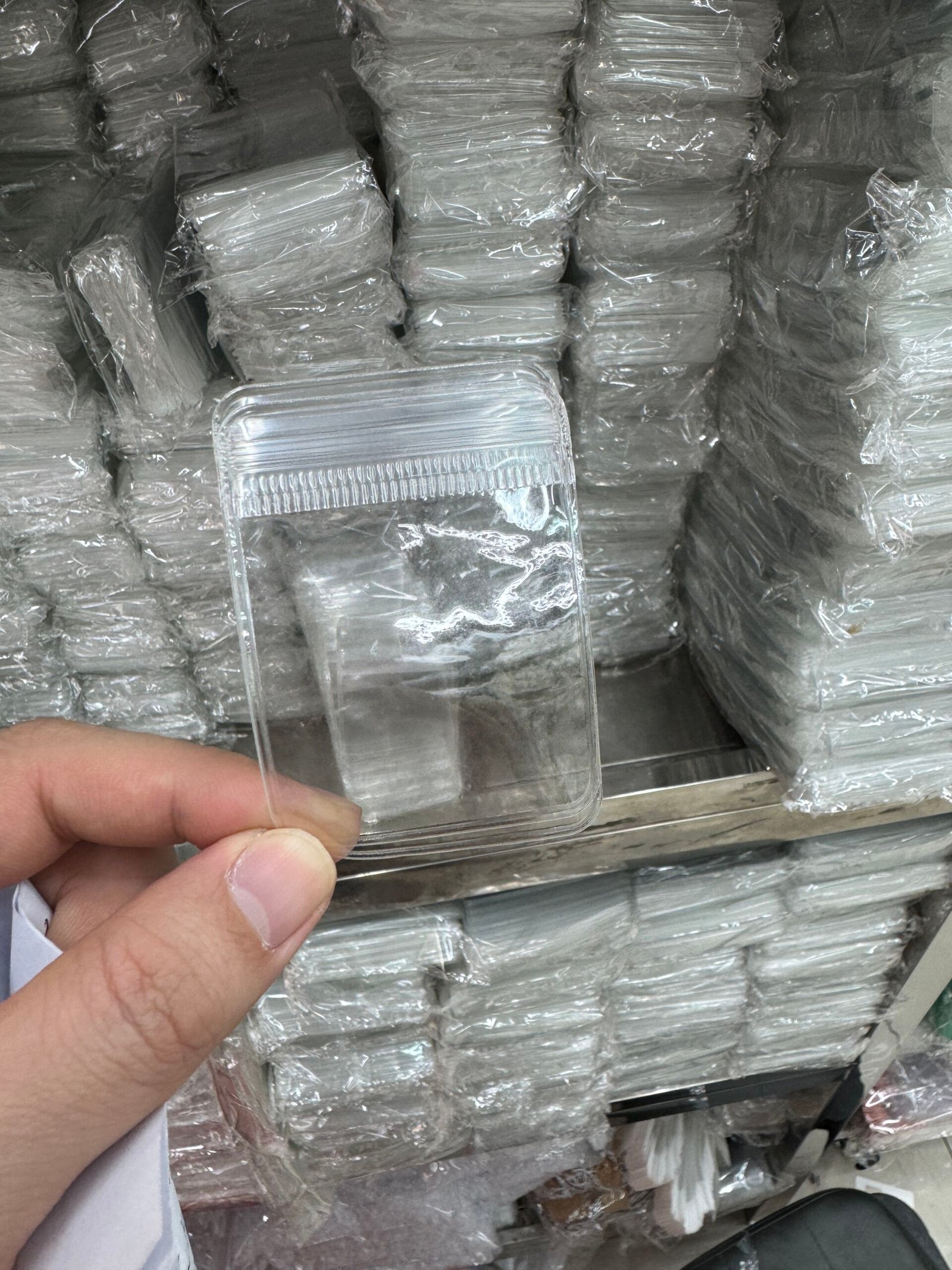 Hand holding a clear PVC jewelry bag, thicker and more protective for delicate accessories and jewelry, with bulk ready stock stacked in the background in Yiwu.