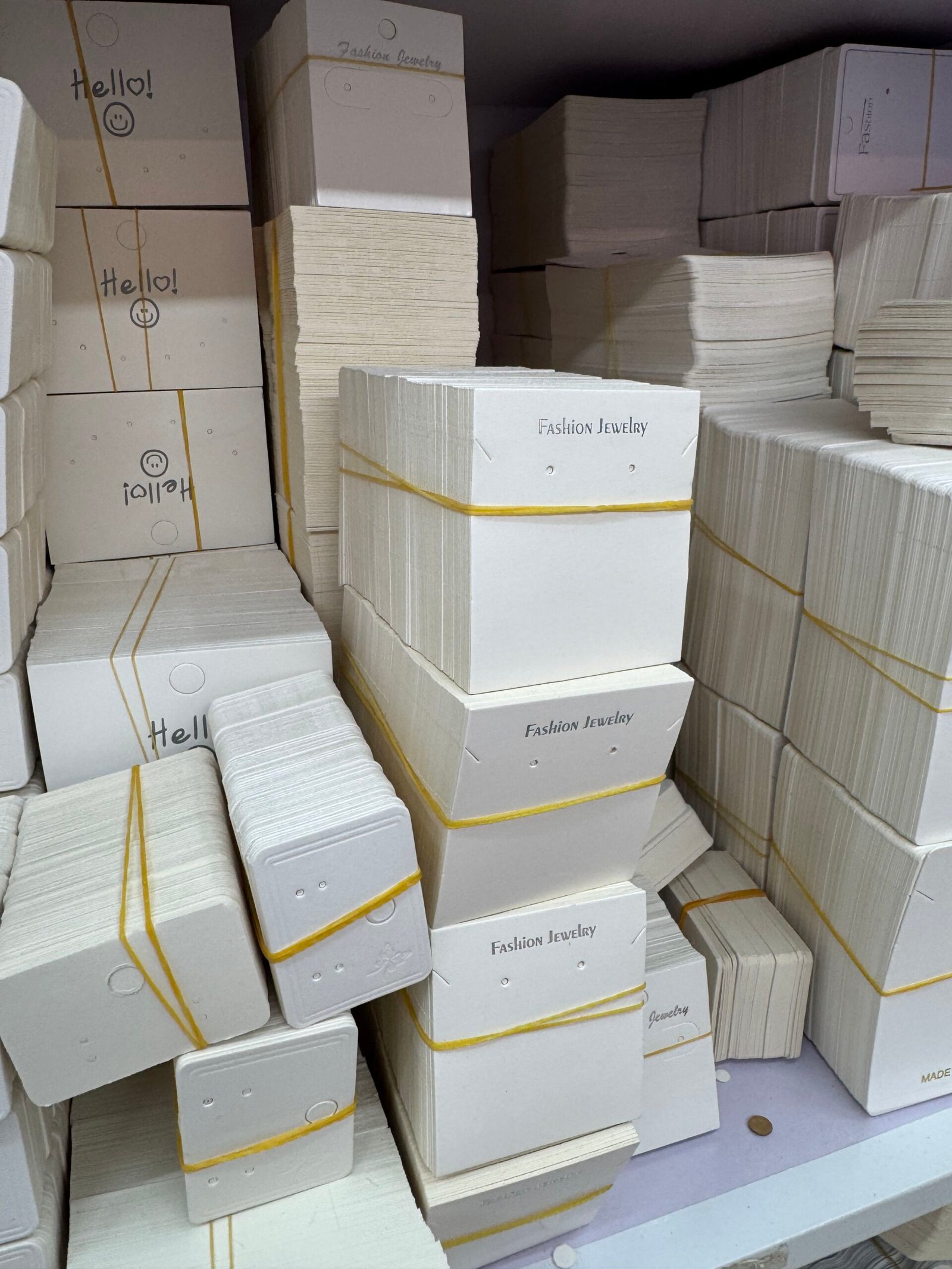 Bundled white jewelry card headers and earring display cards in ready stock, stacked on shelves at a Yiwu supplier store.