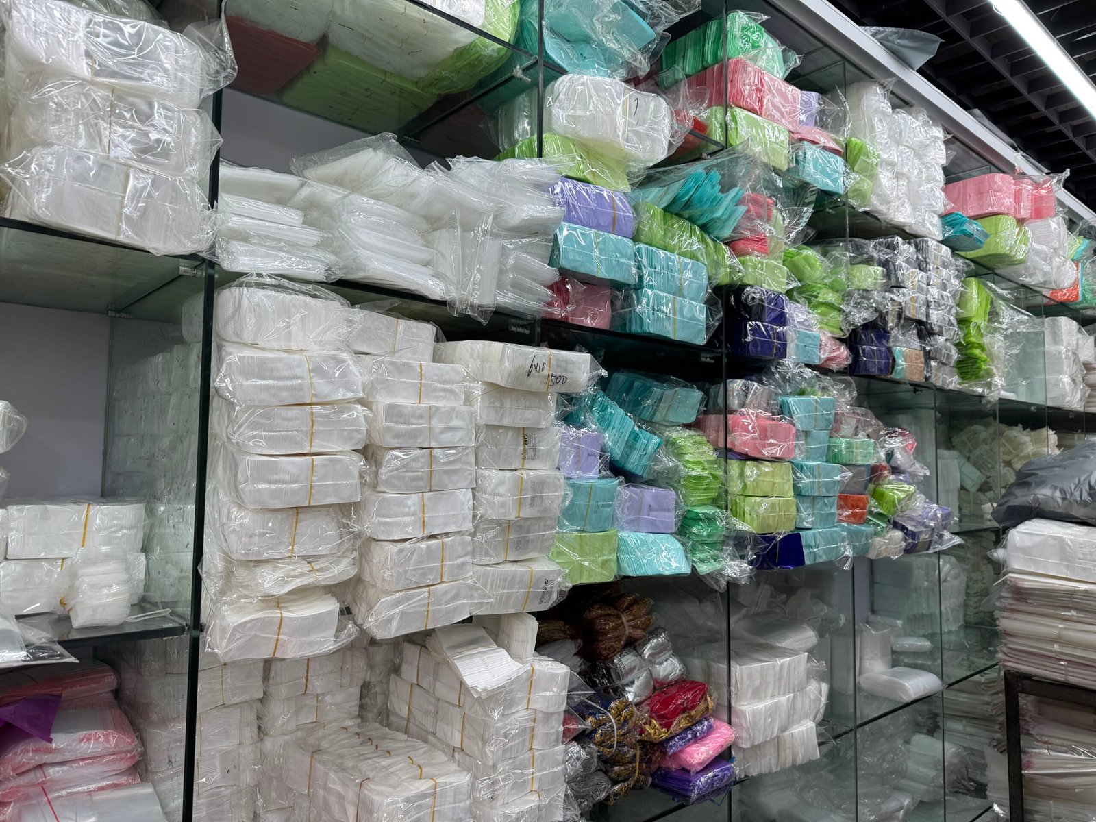 Shelves of macaron-colored jewelry packaging bags bundled in bulk, ready stock available at a Yiwu packaging supplier store.