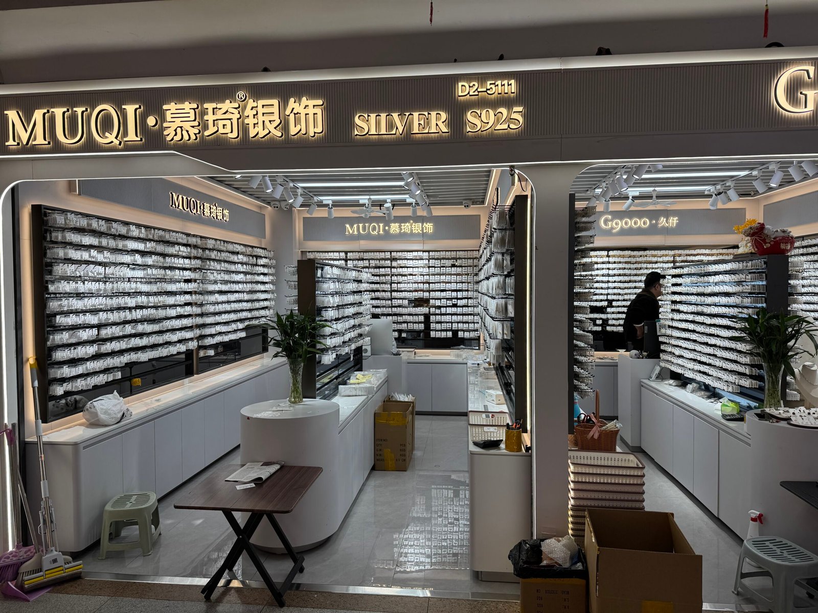 MUQI SILVER S925 shopfront (booth D2-5111) with walls filled with packaged jewelry displays inside Yiwu jewelry wholesale market.