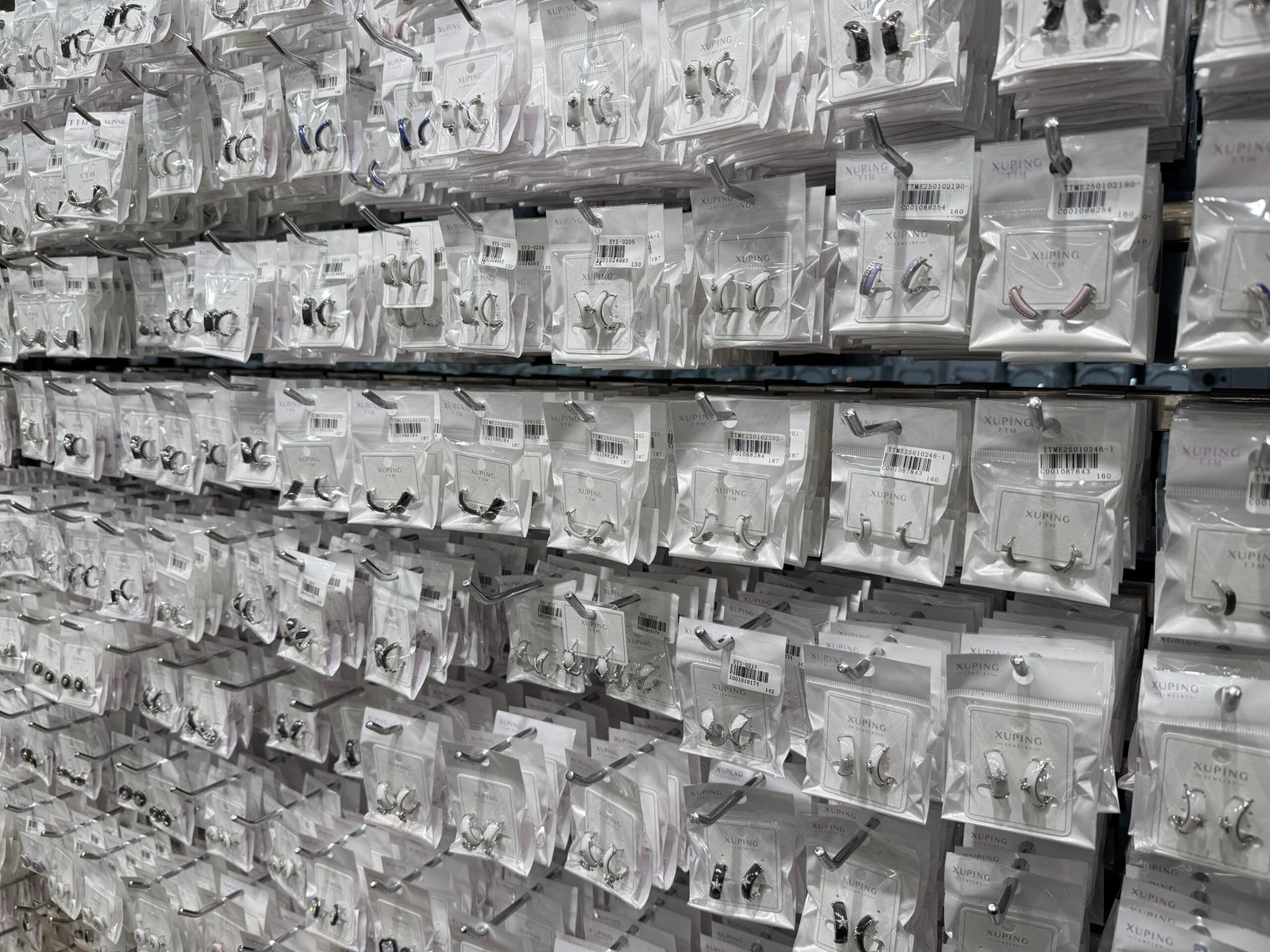 Close-up of XUPING hoop earrings and ear cuffs in clear retail packaging on a wholesale display wall, in Yiwu Jewelry Market