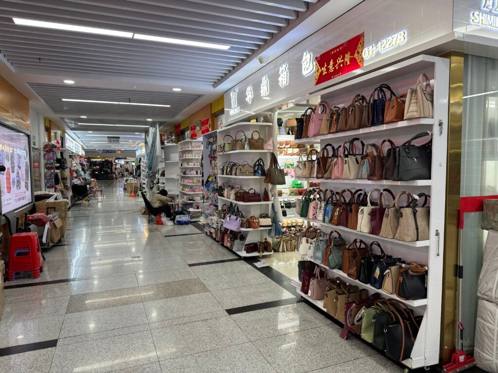 Women’s handbag shop in Yiwu wholesale market with shelves packed with totes, satchels, and crossbody bags, photographed along a bright indoor corridor.