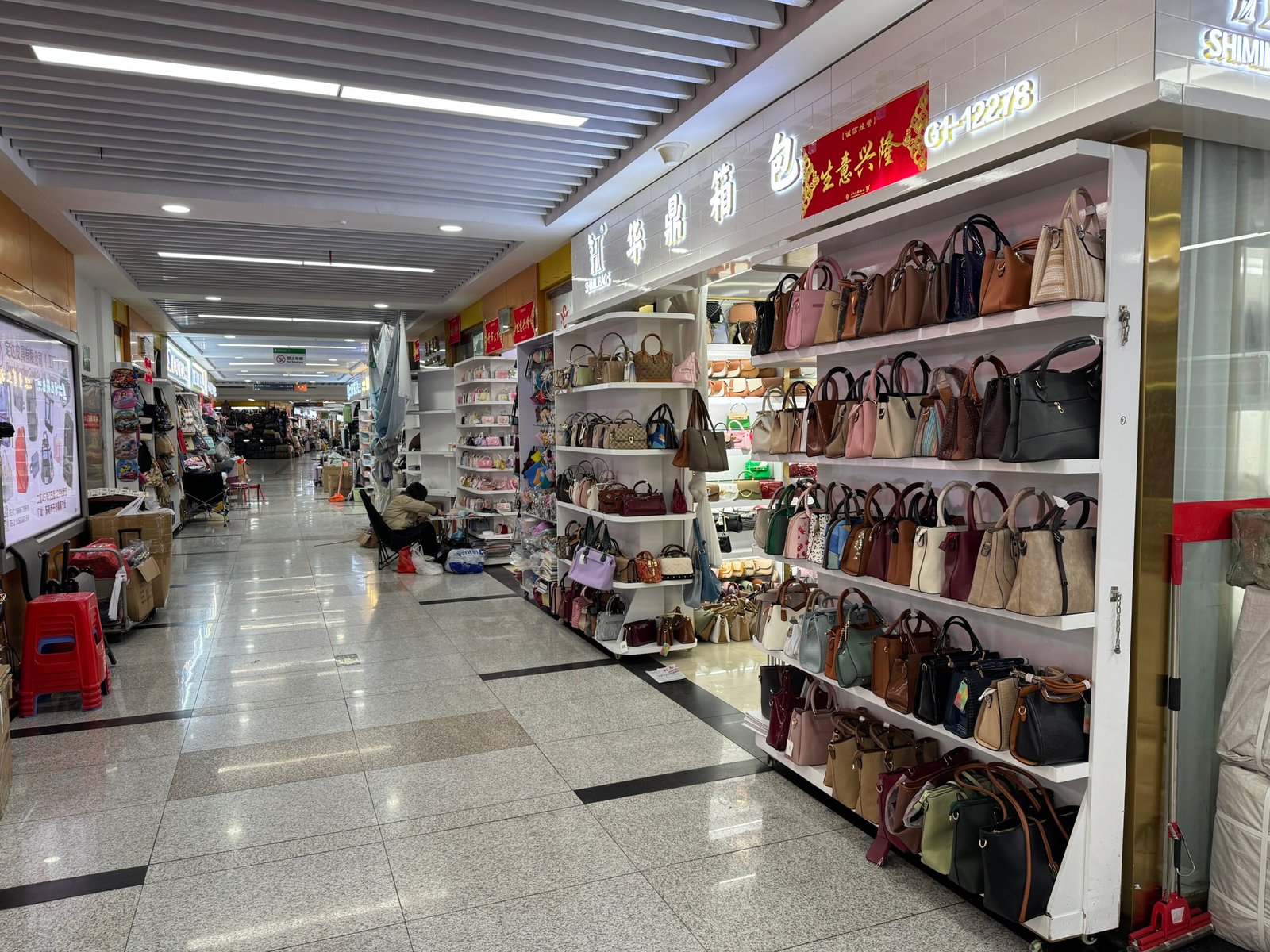 Women’s handbag shop in Yiwu wholesale market with shelves packed with totes, satchels, and crossbody bags, photographed along a bright indoor corridor.