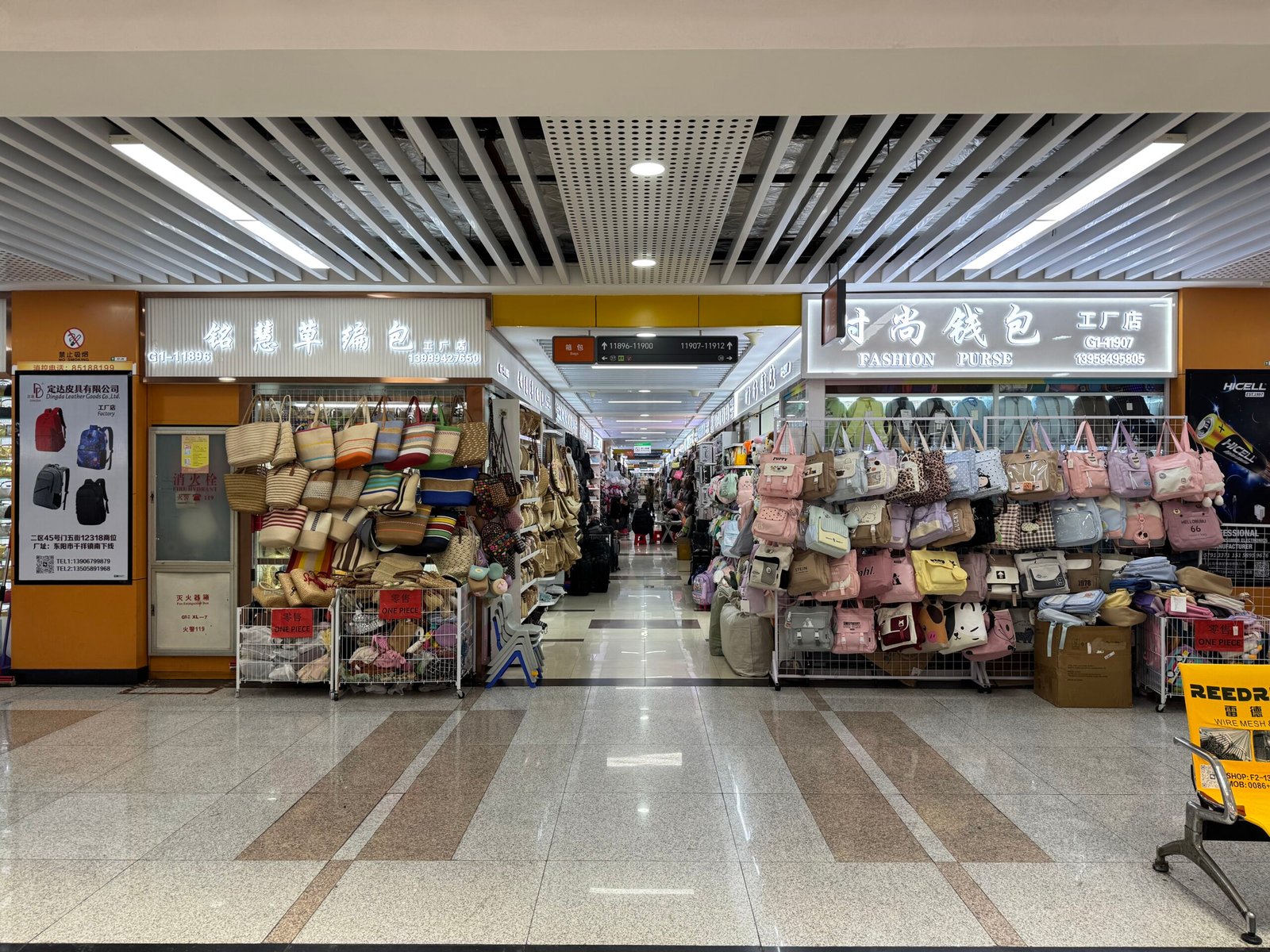Handbag wholesale aisle entrance in Yiwu market showing fashion purse shops, straw tote bags on the left, and pastel women’s handbags and mini bags on hanging racks.