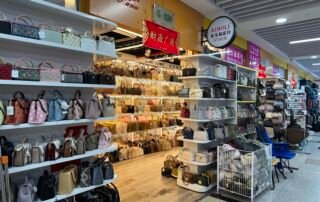 AIMOLI handbag wholesale shop in Yiwu bag wholesale market with shelves filled with women’s purses, including top-handle bags, mini handbags, and structured totes.